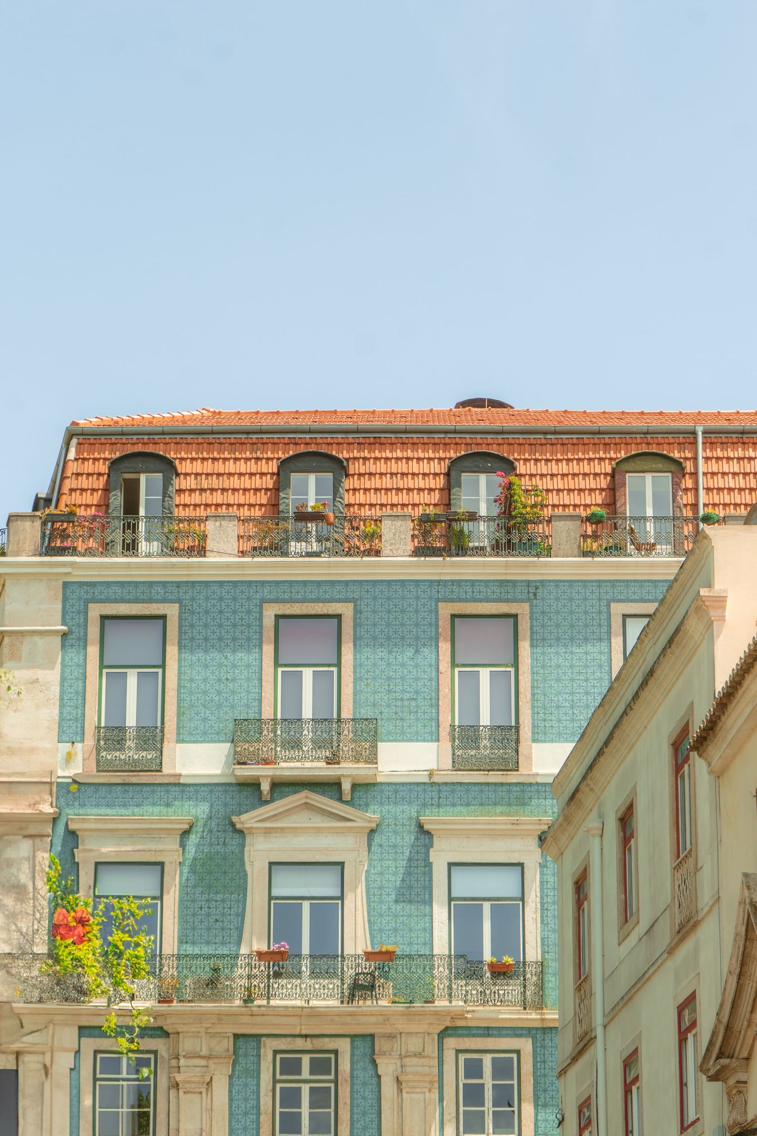 Historic Portuguese apartment building with turquoise tile facade and terracotta roof tiles on a sunny day.