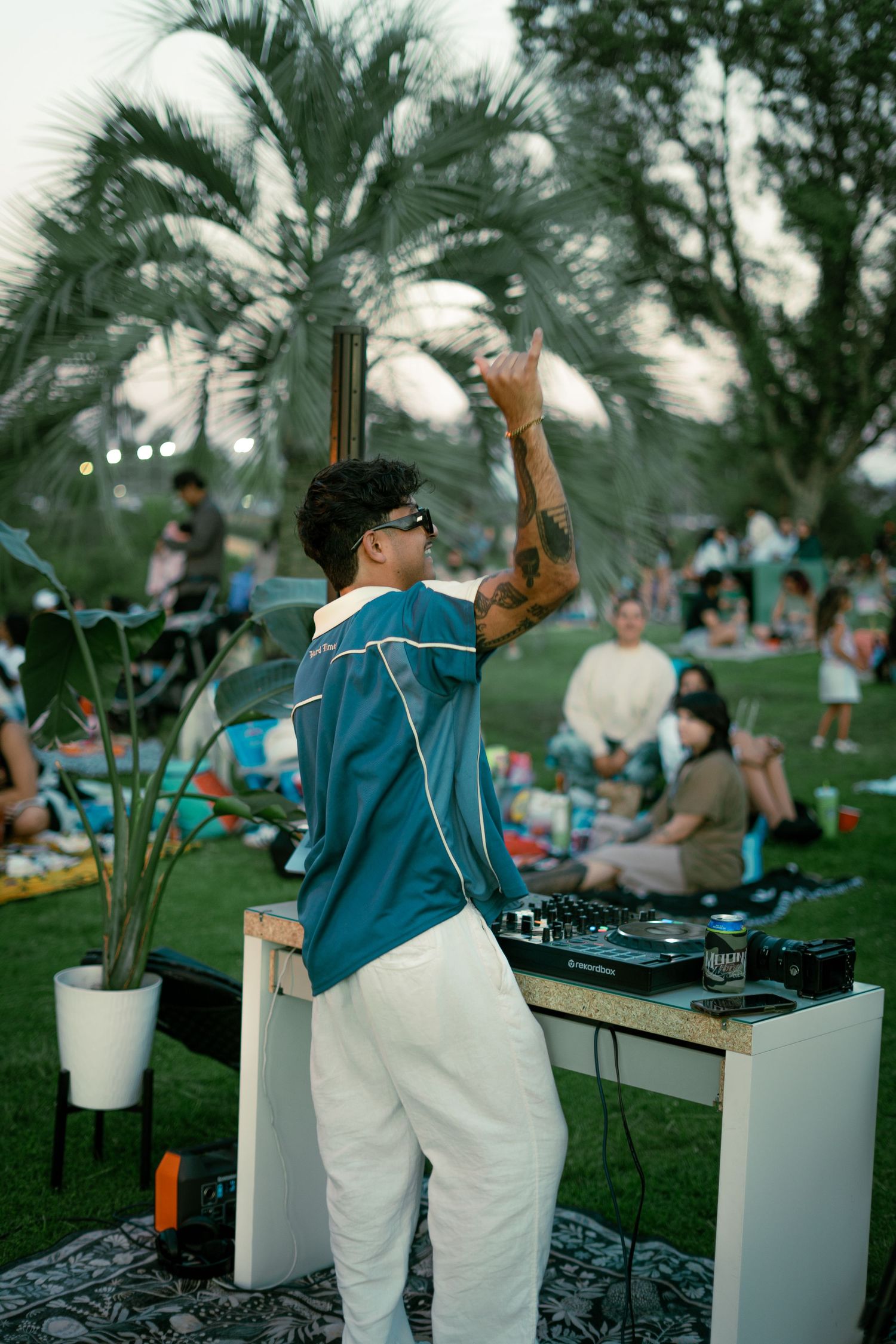 DJ performing at outdoor event with palm trees and white decor elements.