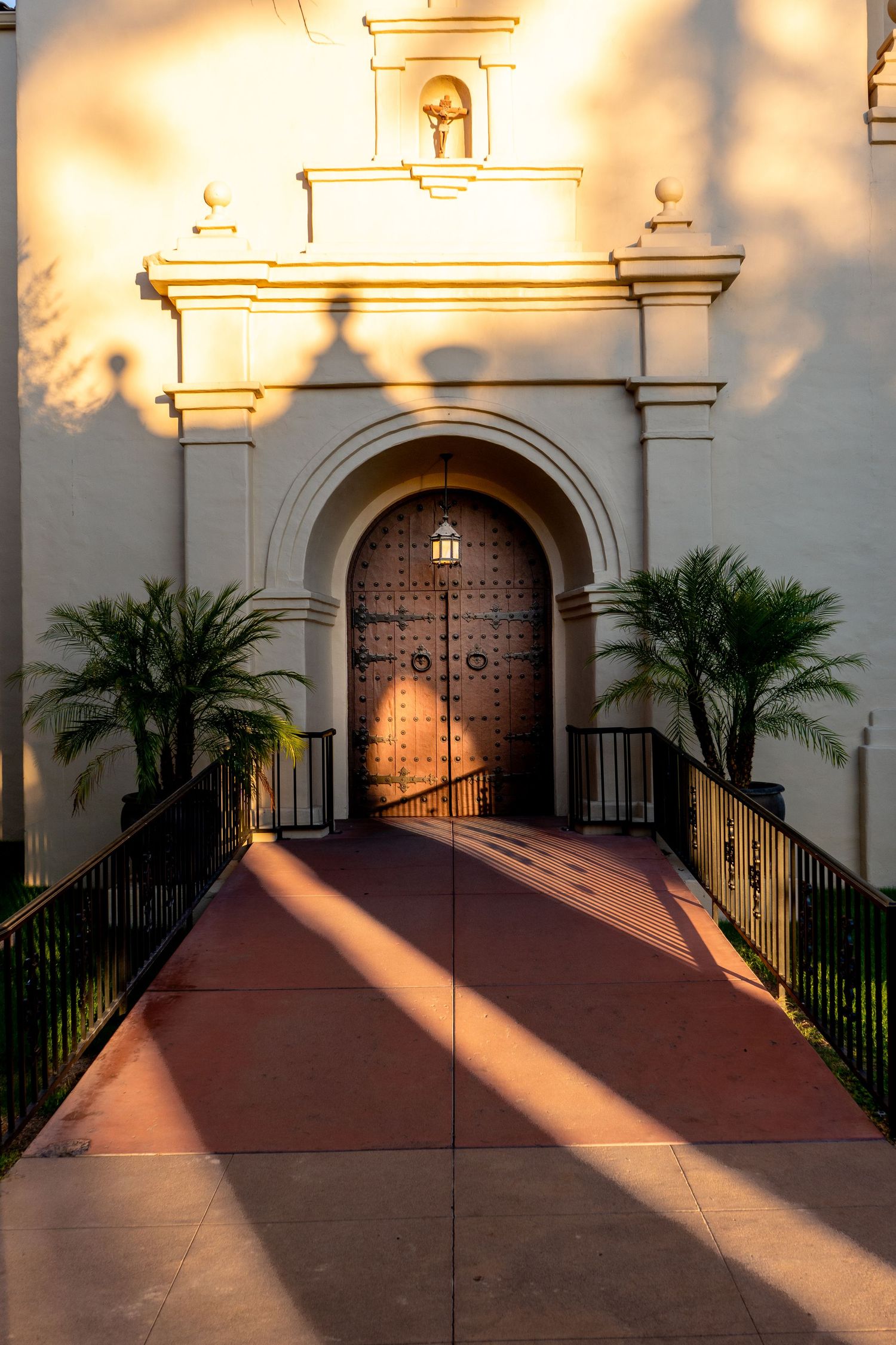 White church entrance with palm trees and dramatic shadow patterns at sunset.