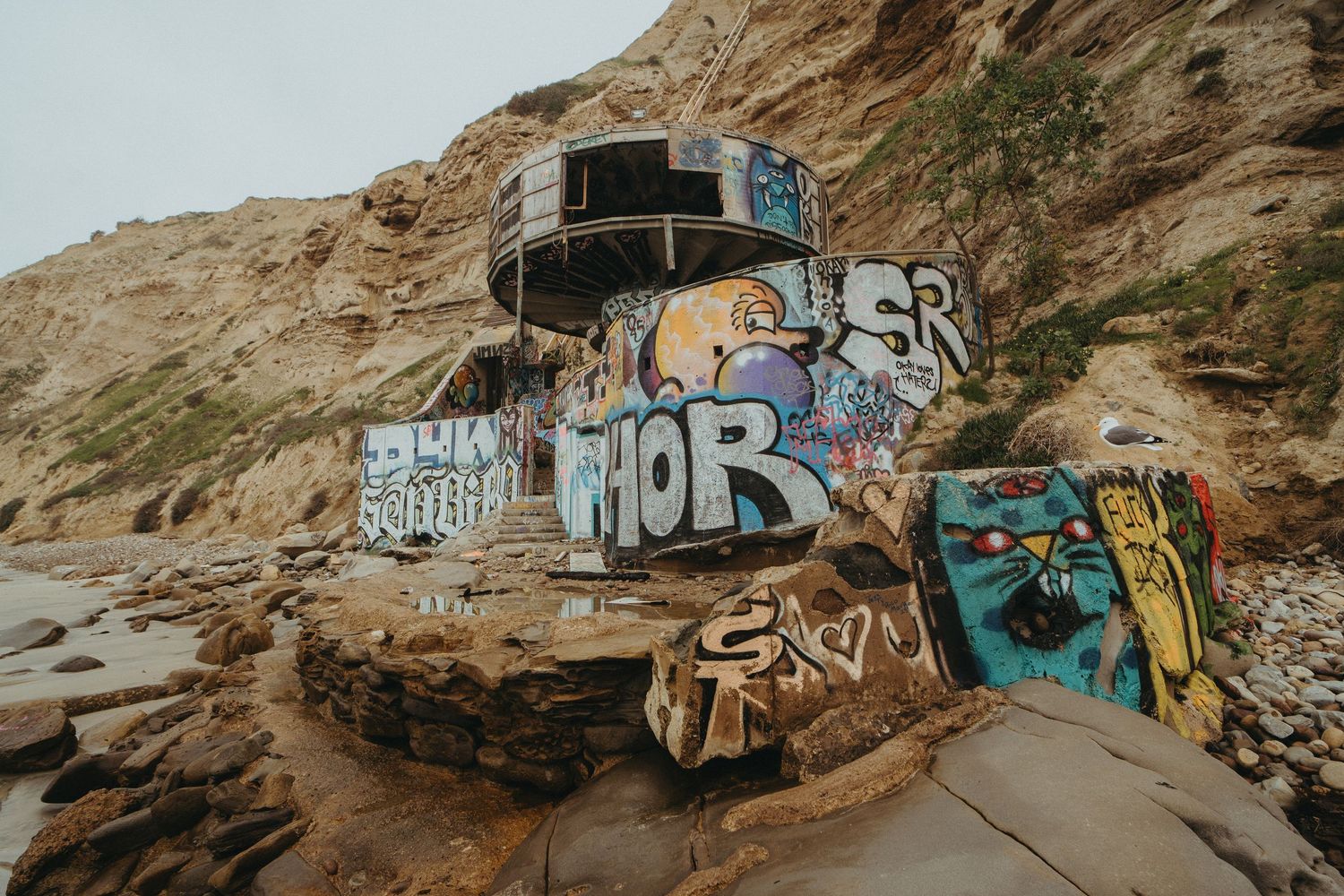 Colorful graffiti art covers large rocks and boulders along a desert cliff face creating an outdoor gallery space.