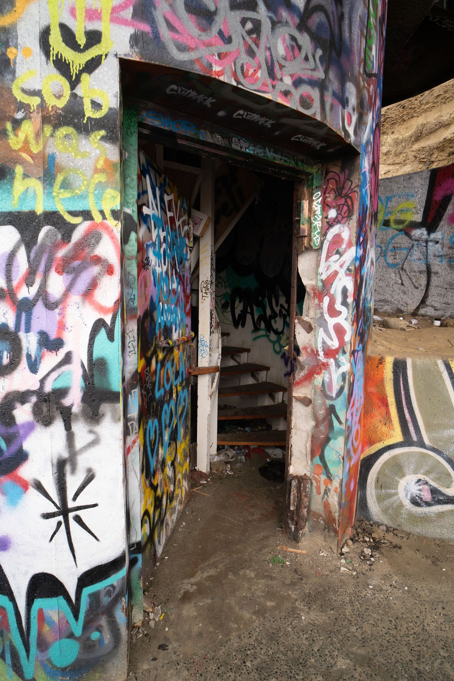Graffiti-covered concrete tunnel walls with colorful street art and tags in an urban underground passageway.