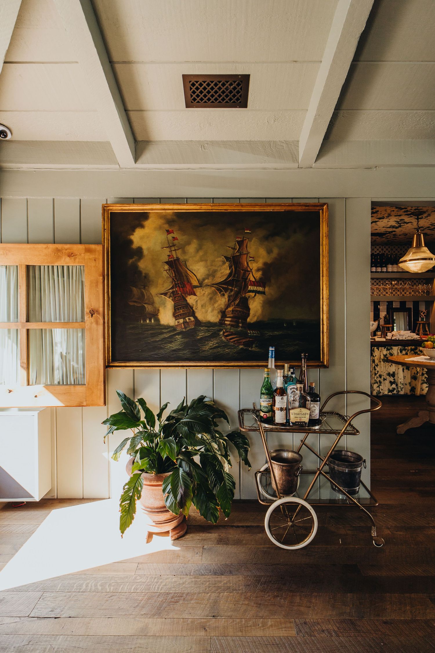 Converted attic space with rustic wood floors, white paneled walls, and vintage artwork featuring maritime scenes.
