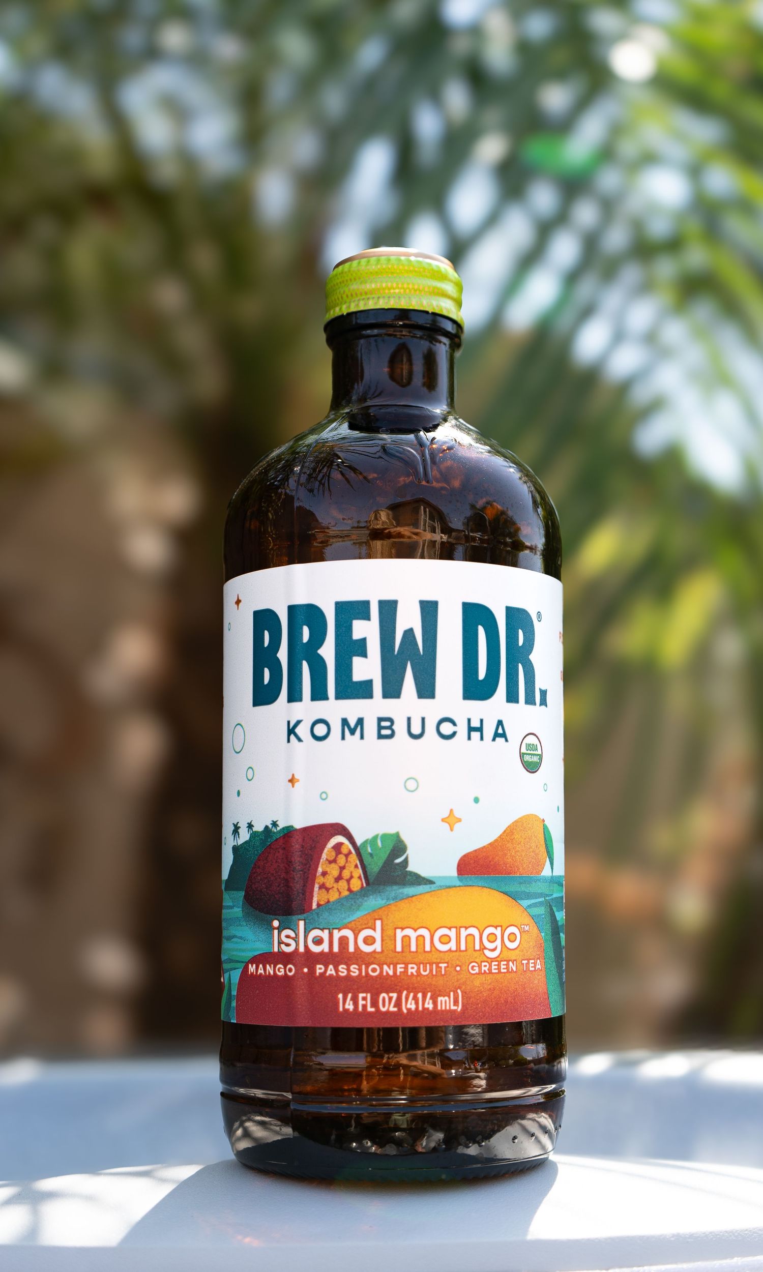 Brew Dr. Kombucha Island Mango flavor bottle showcased against a tropical blurred background.