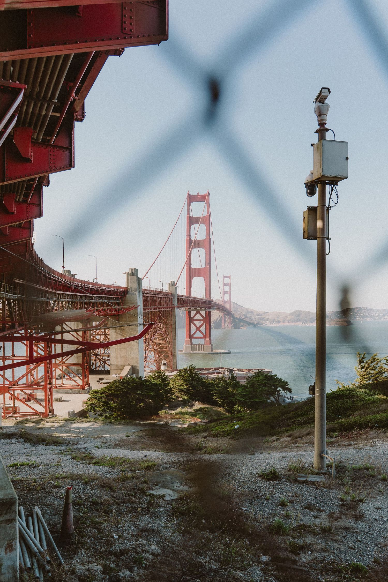 View of the iconic Golden Gate Bridge through chain-link fence in San Francisco on a misty morning.