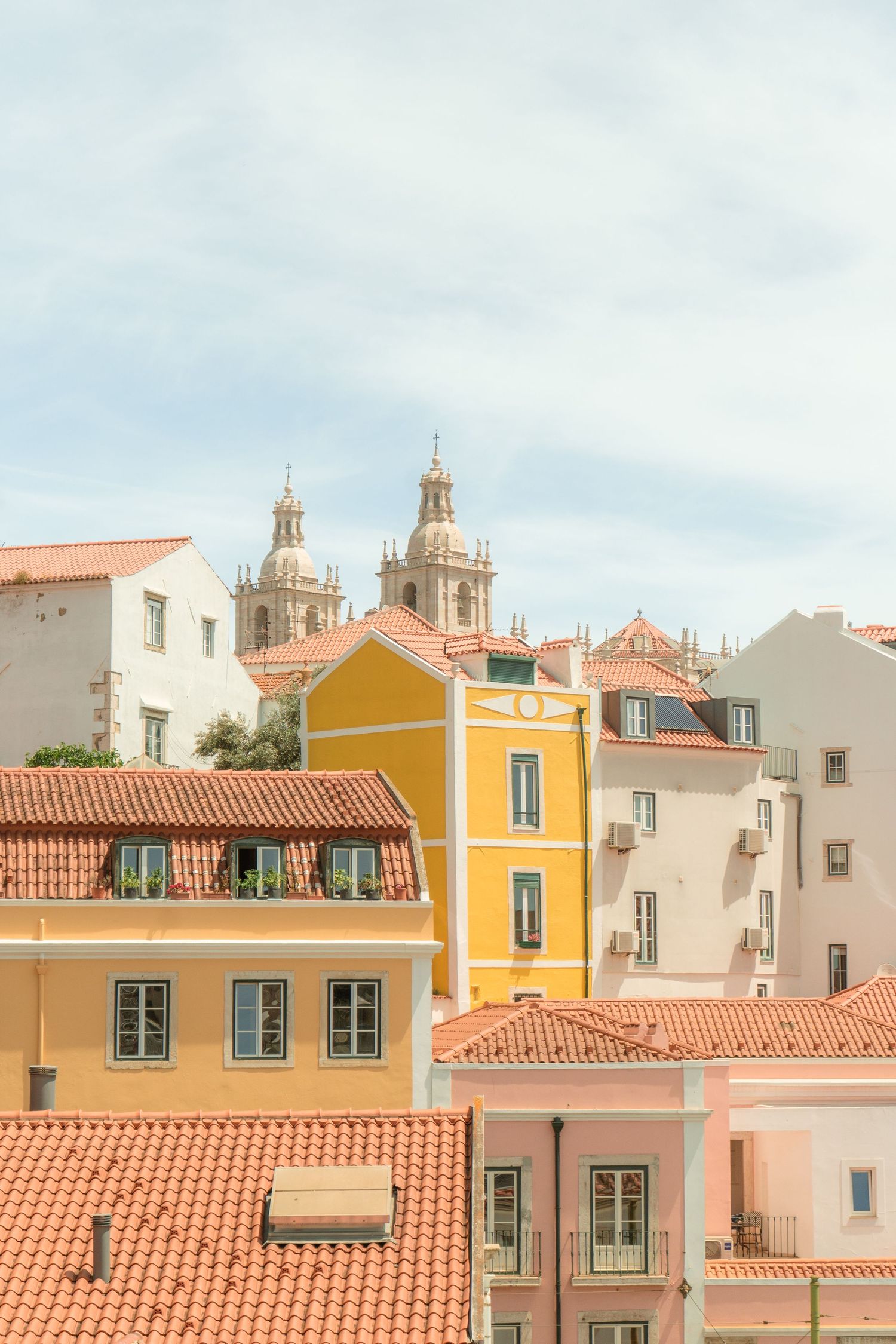 Pastel colored Mediterranean buildings with orange terracotta roofs and church domes peeking over the skyline in Lisbon.