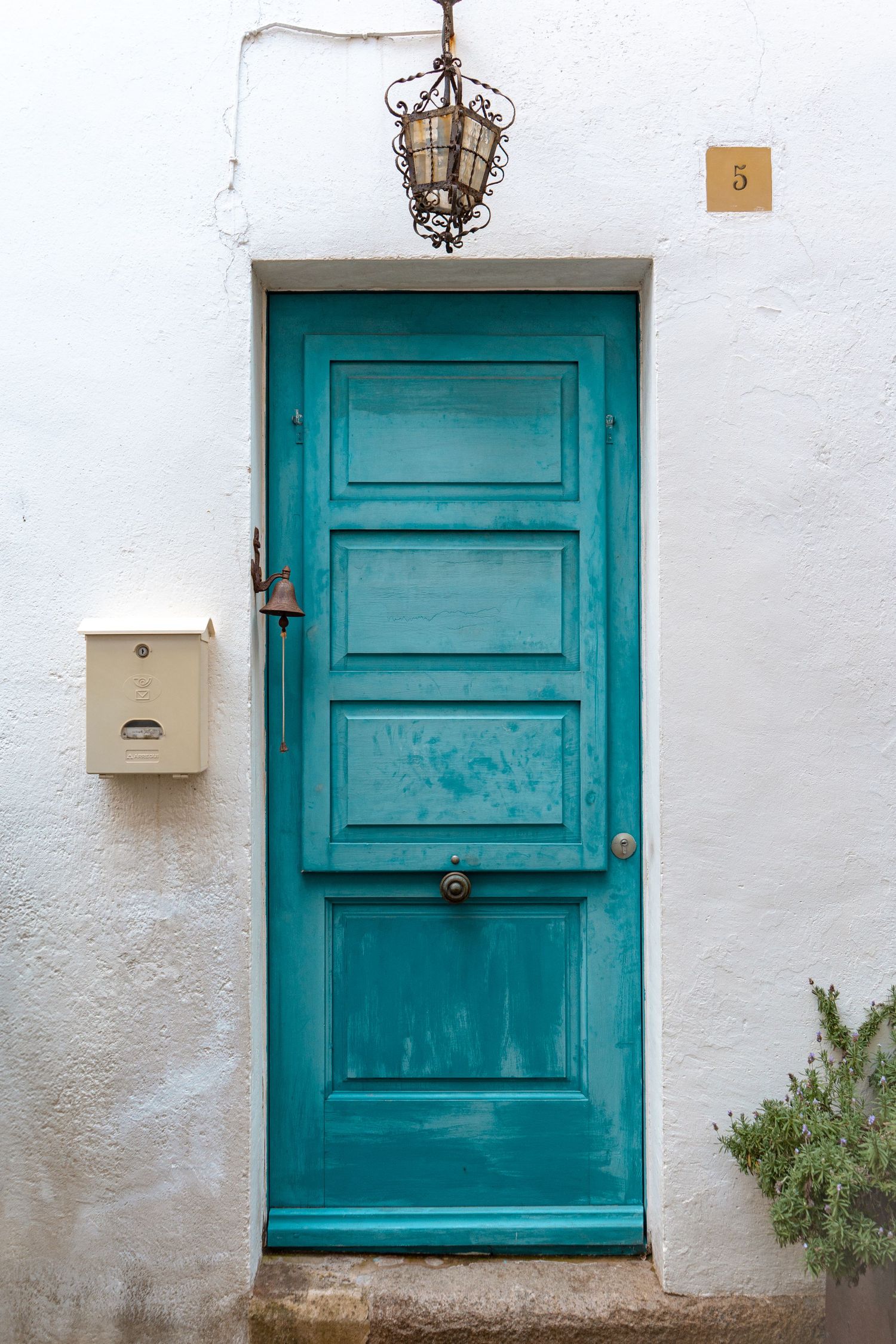 Vintage turquoise wooden door with decorative metal lantern on white stucco wall marked with number 9.