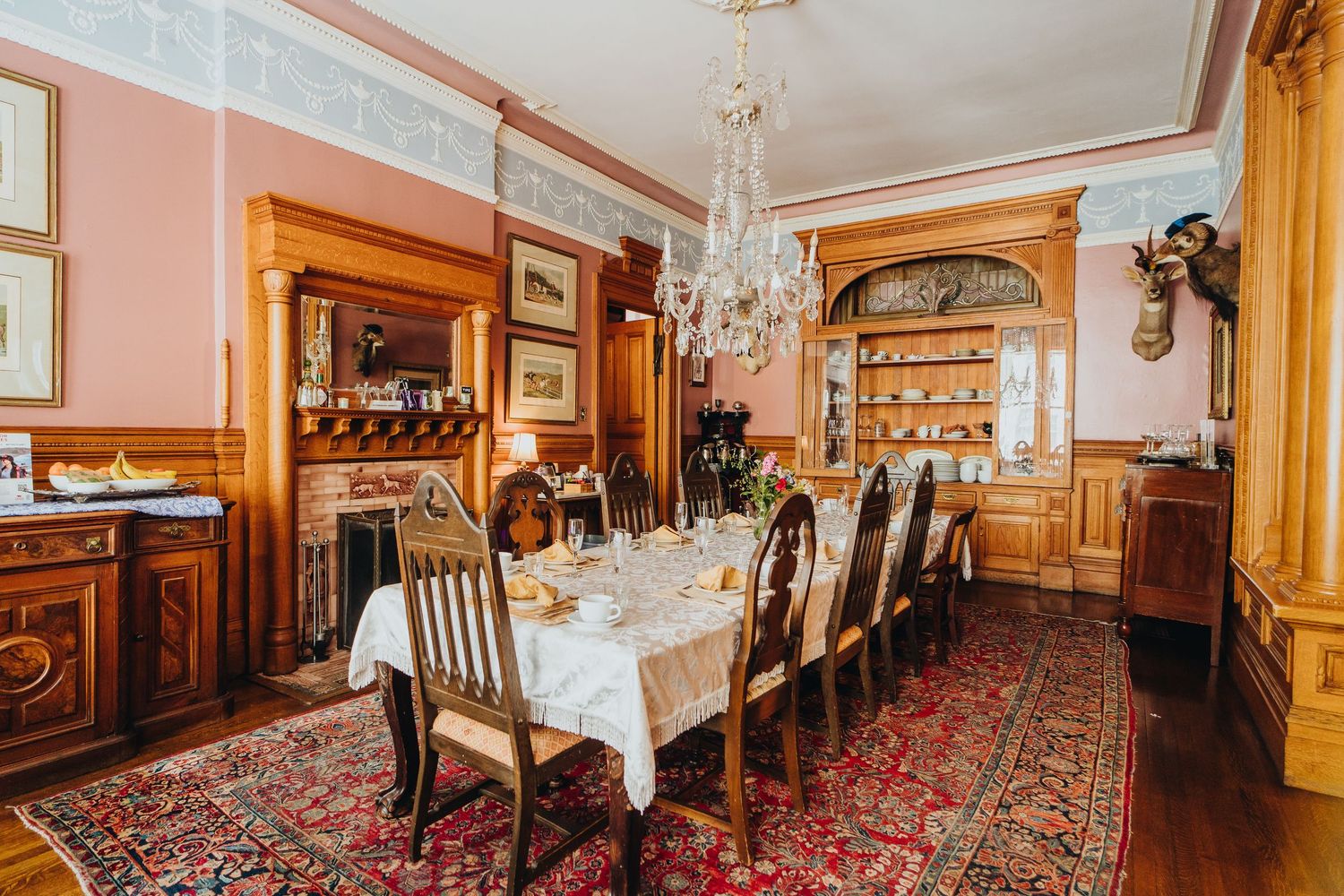 Elegant Victorian-era hallway with ornate crystal chandelier, vintage wooden furniture, and patterned red carpet runner.