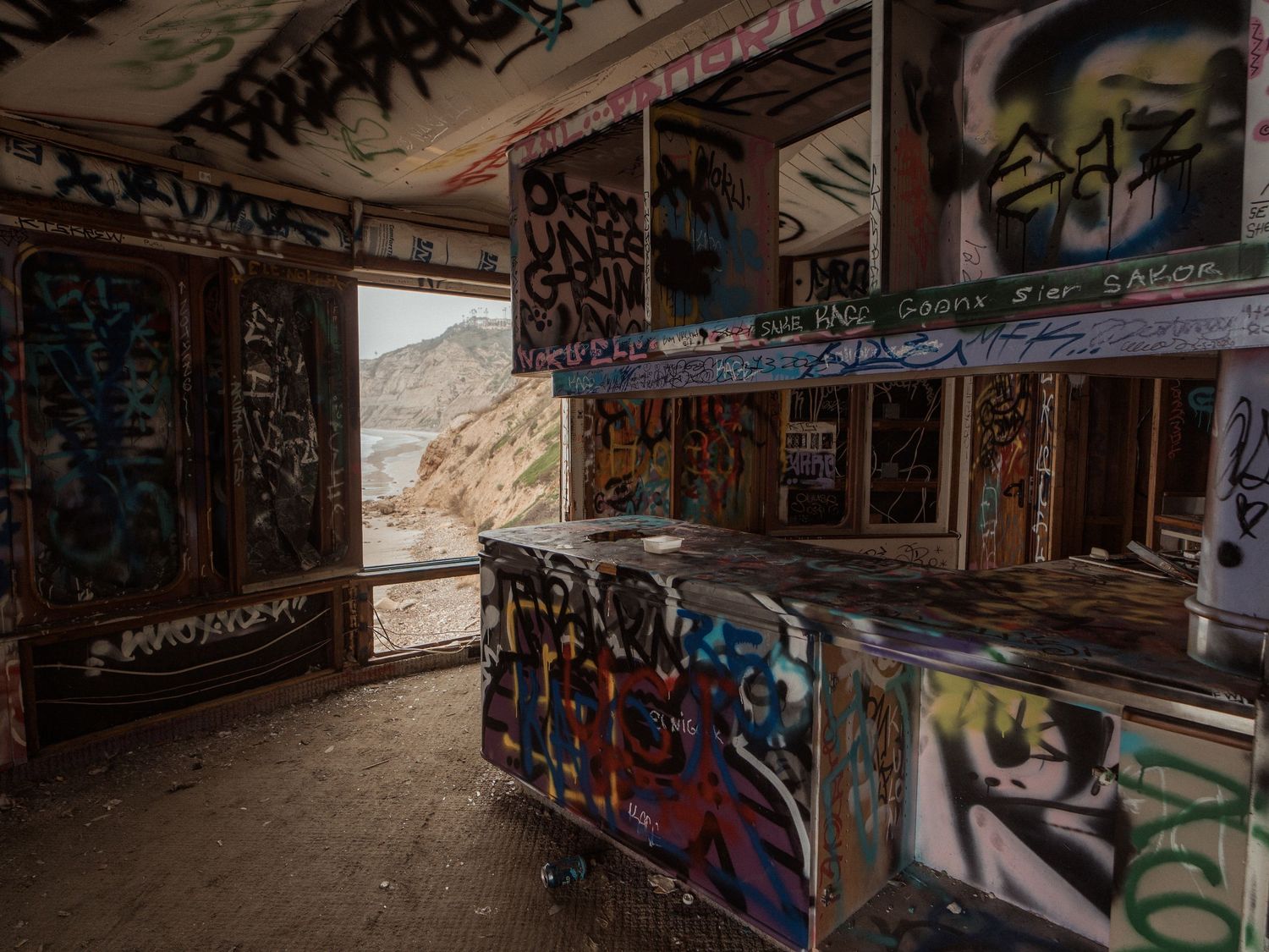 Abandoned interior room covered in colorful graffiti with mountain view through window opening.