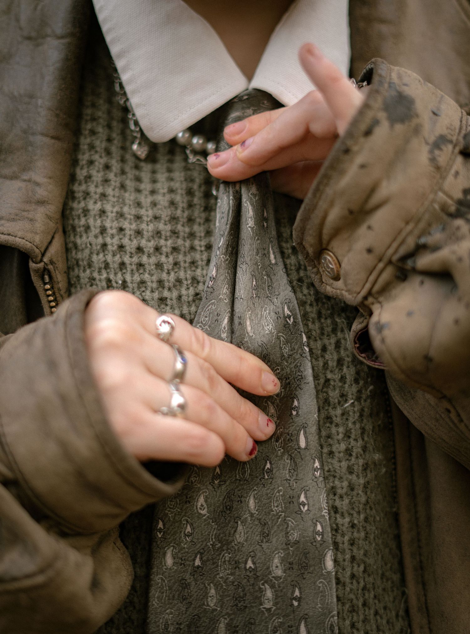 Close-up of hands wearing rings holding a vintage bottle covered in raindrops against a knit sweater and jacket.