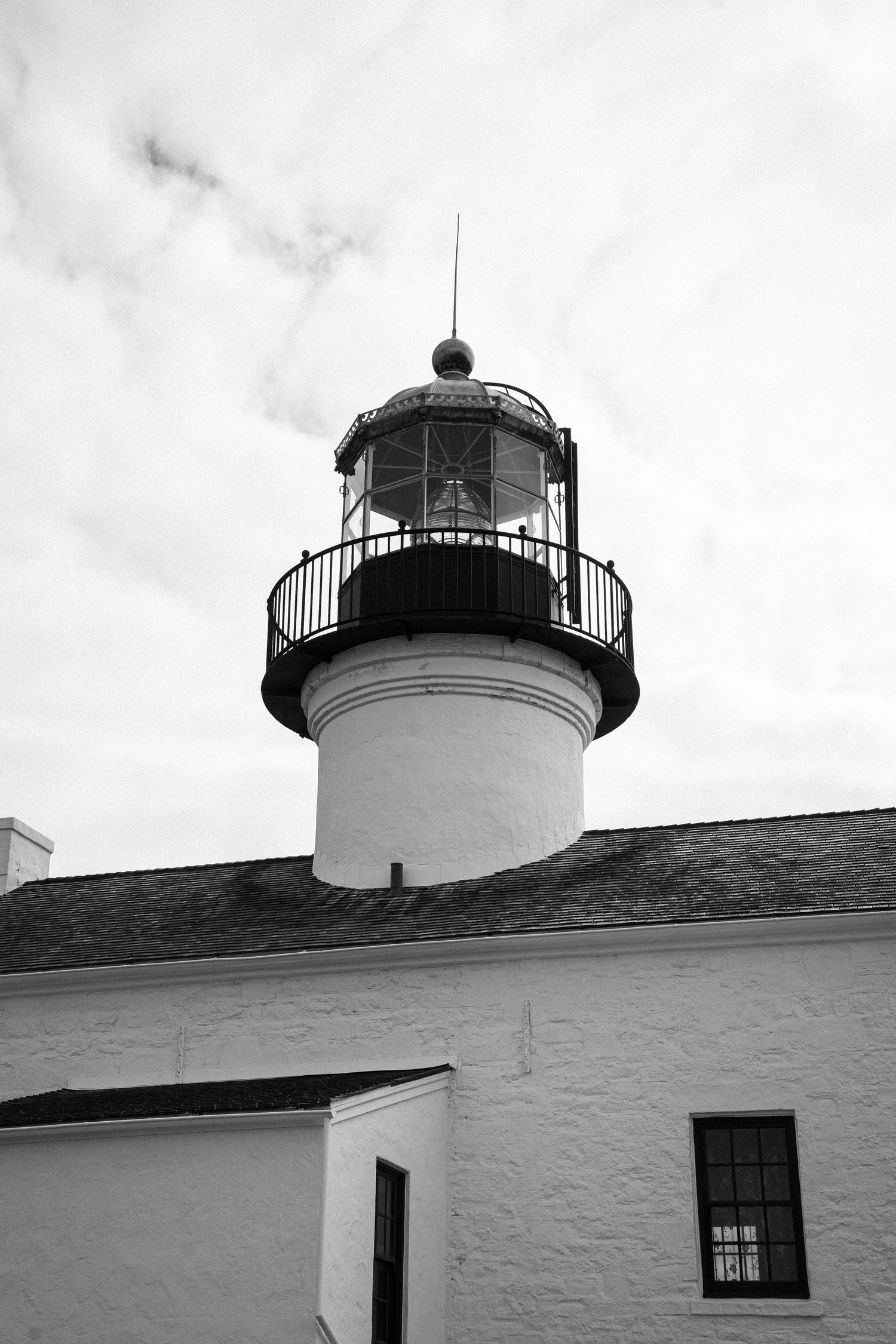 Close-up view of the Point Loma Lighthouse tower and white walls against a cloudy sky in San Diego.