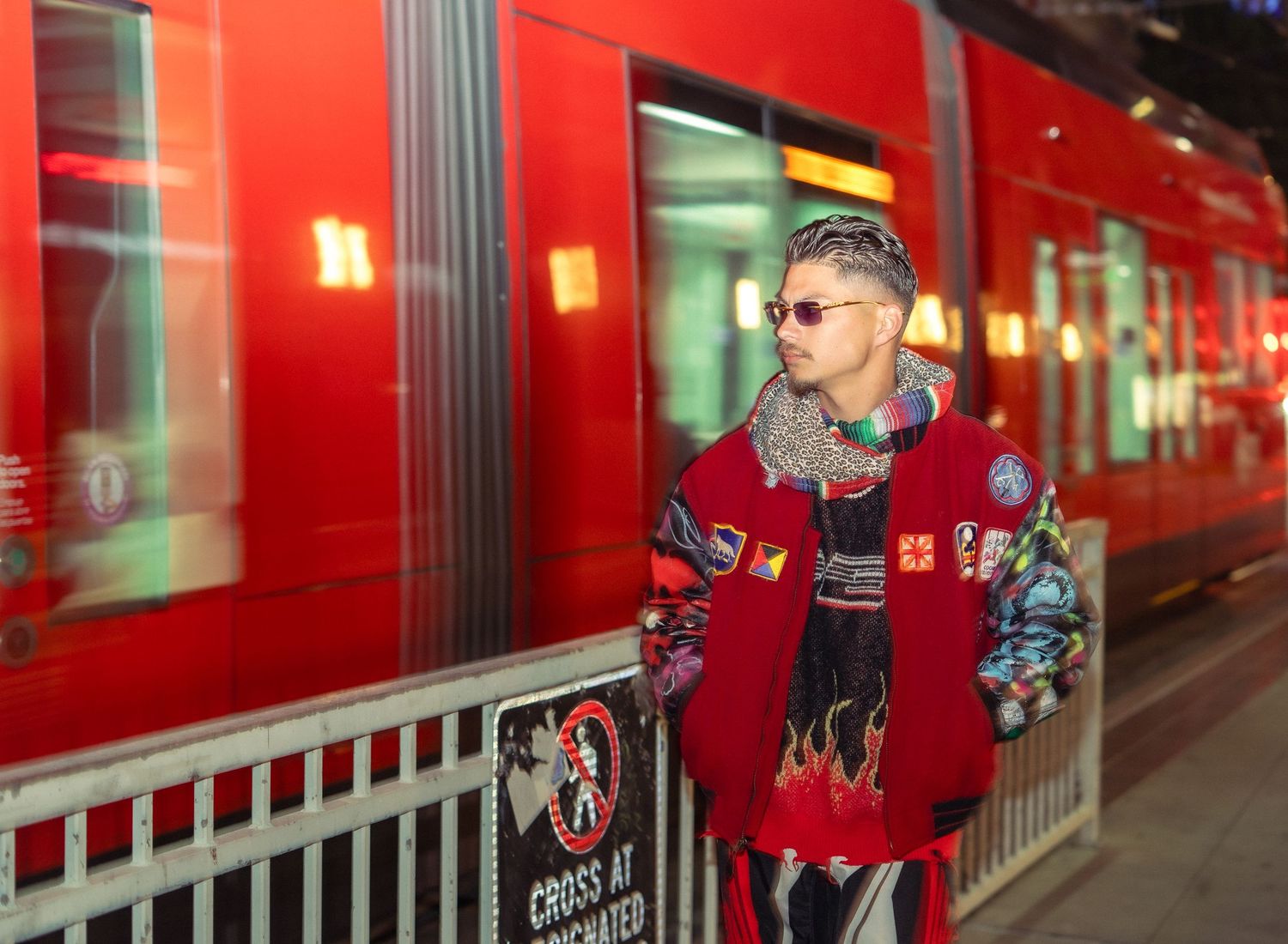 Urban fashion photoshoot against red transit train with green-lit windows in background.