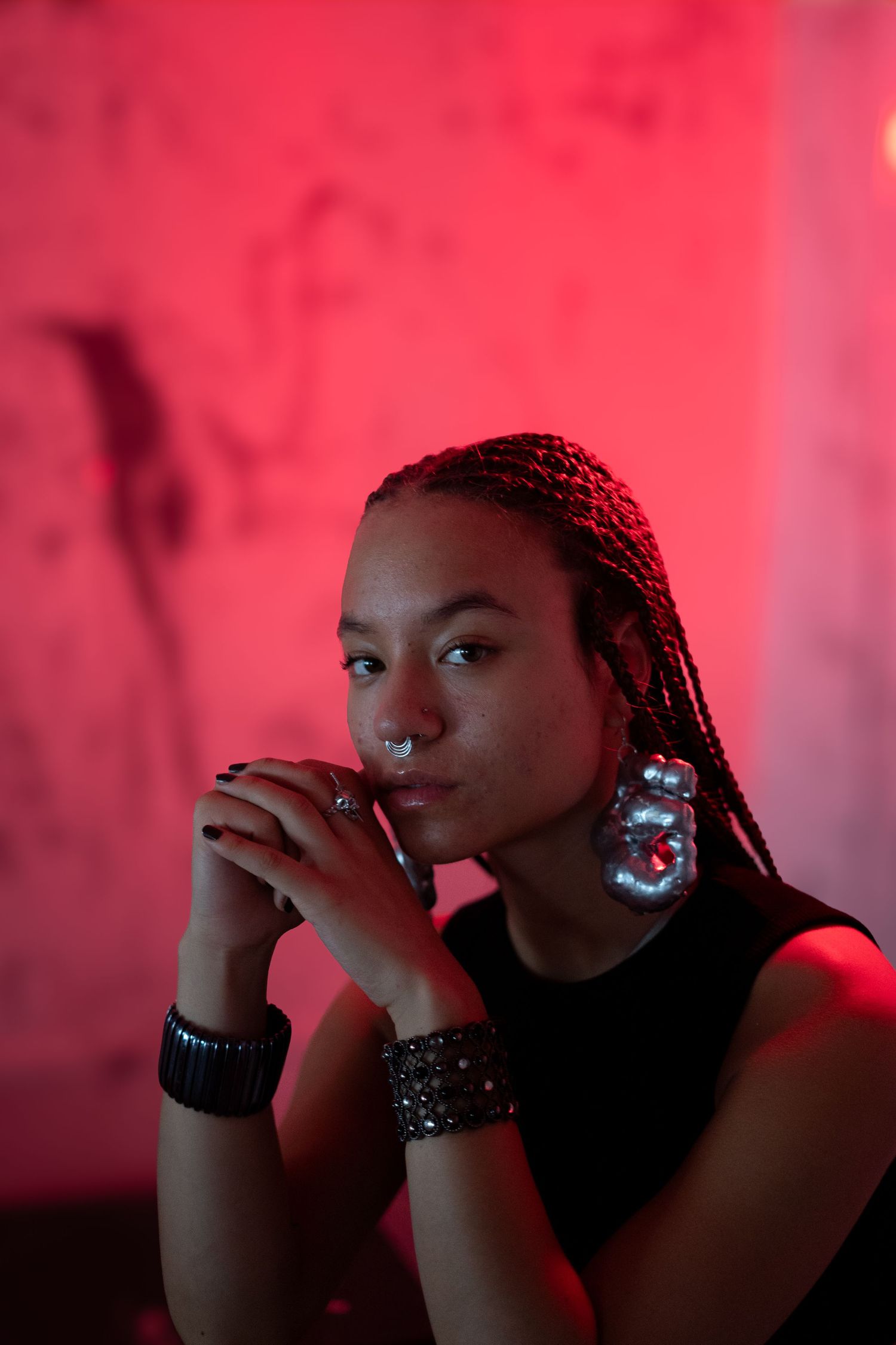 Atmospheric portrait in red lighting featuring braided hair and statement jewelry.