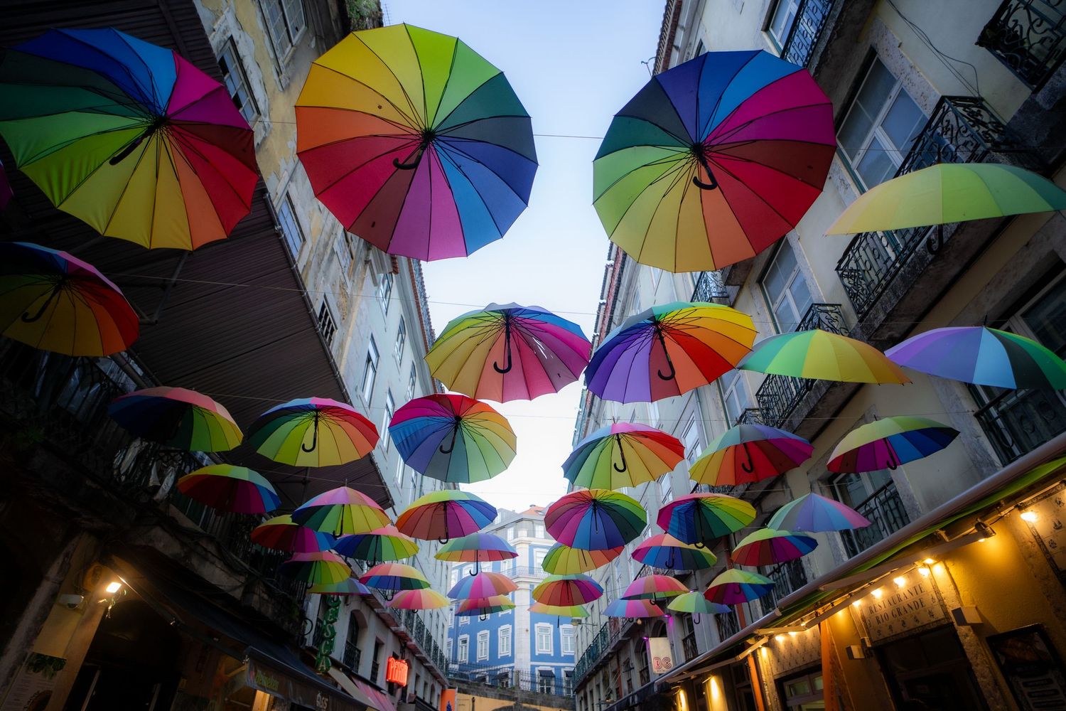 Colorful rainbow umbrellas hanging above city street creating artistic canopy.