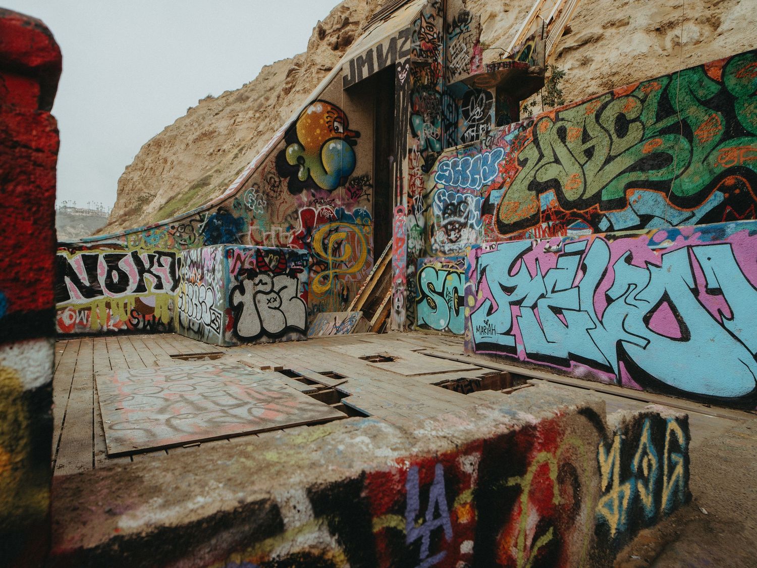 Colorful graffiti art covers the walls of a curved concrete tunnel with natural rock formations visible above.