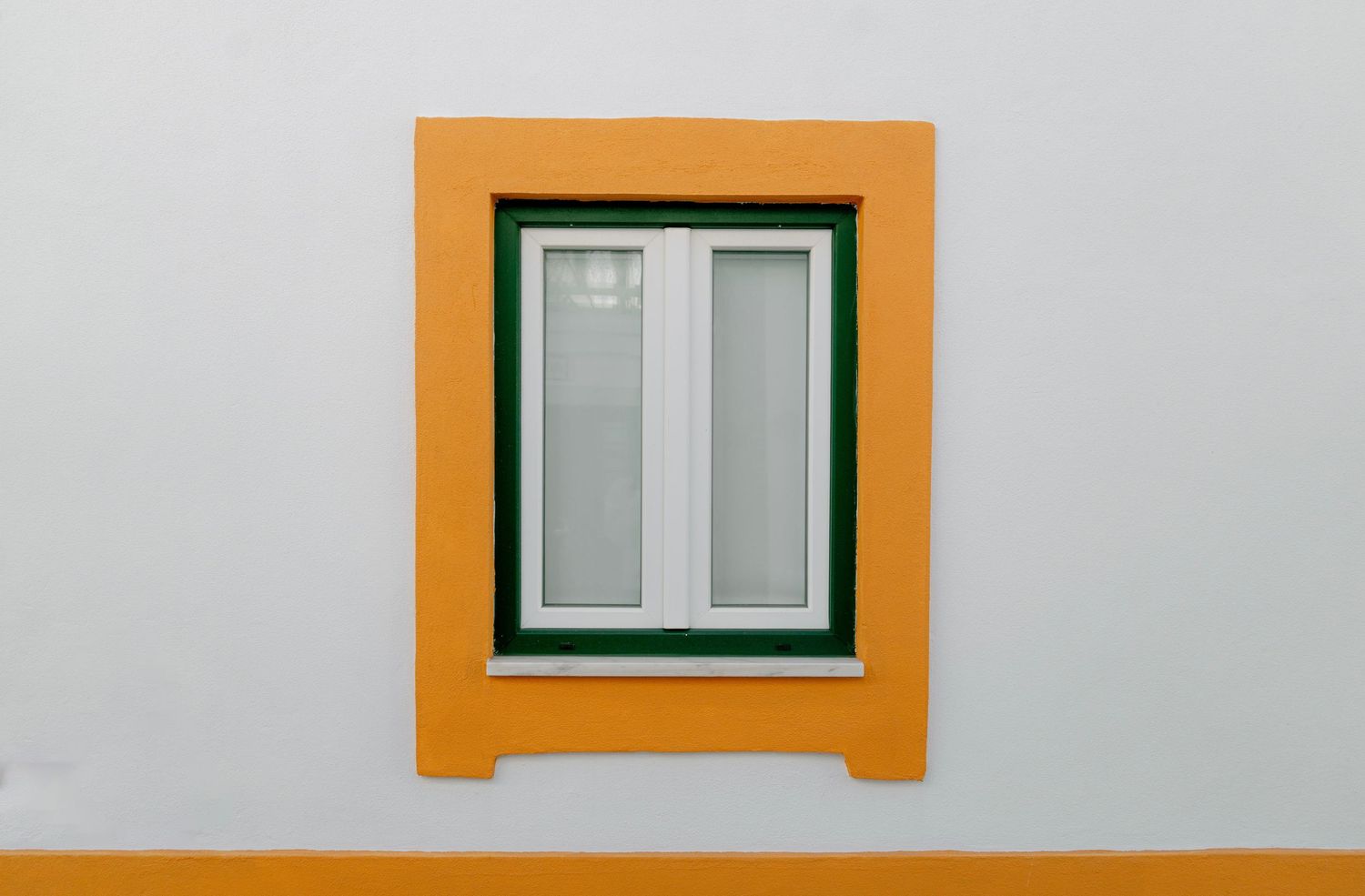 A row of windows with orange trim and green frames on a white stucco wall creates a geometric architectural pattern.