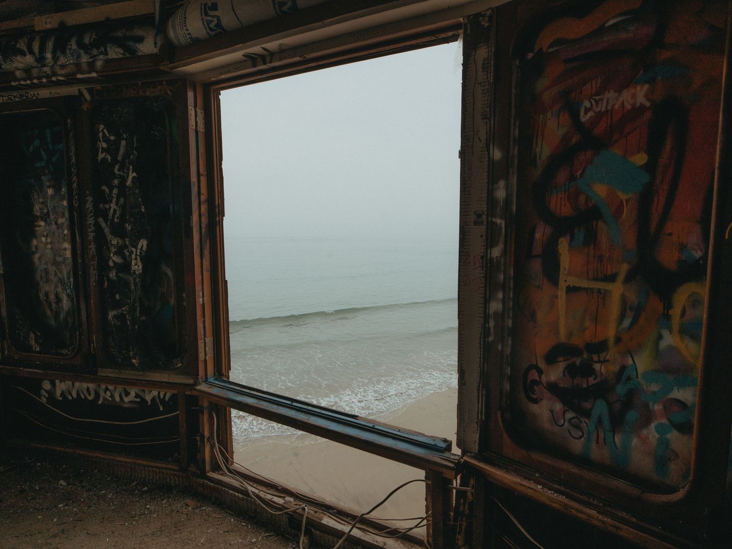 A series of vintage train car windows with weathered frames and graffiti showing views of the ocean and landscape.