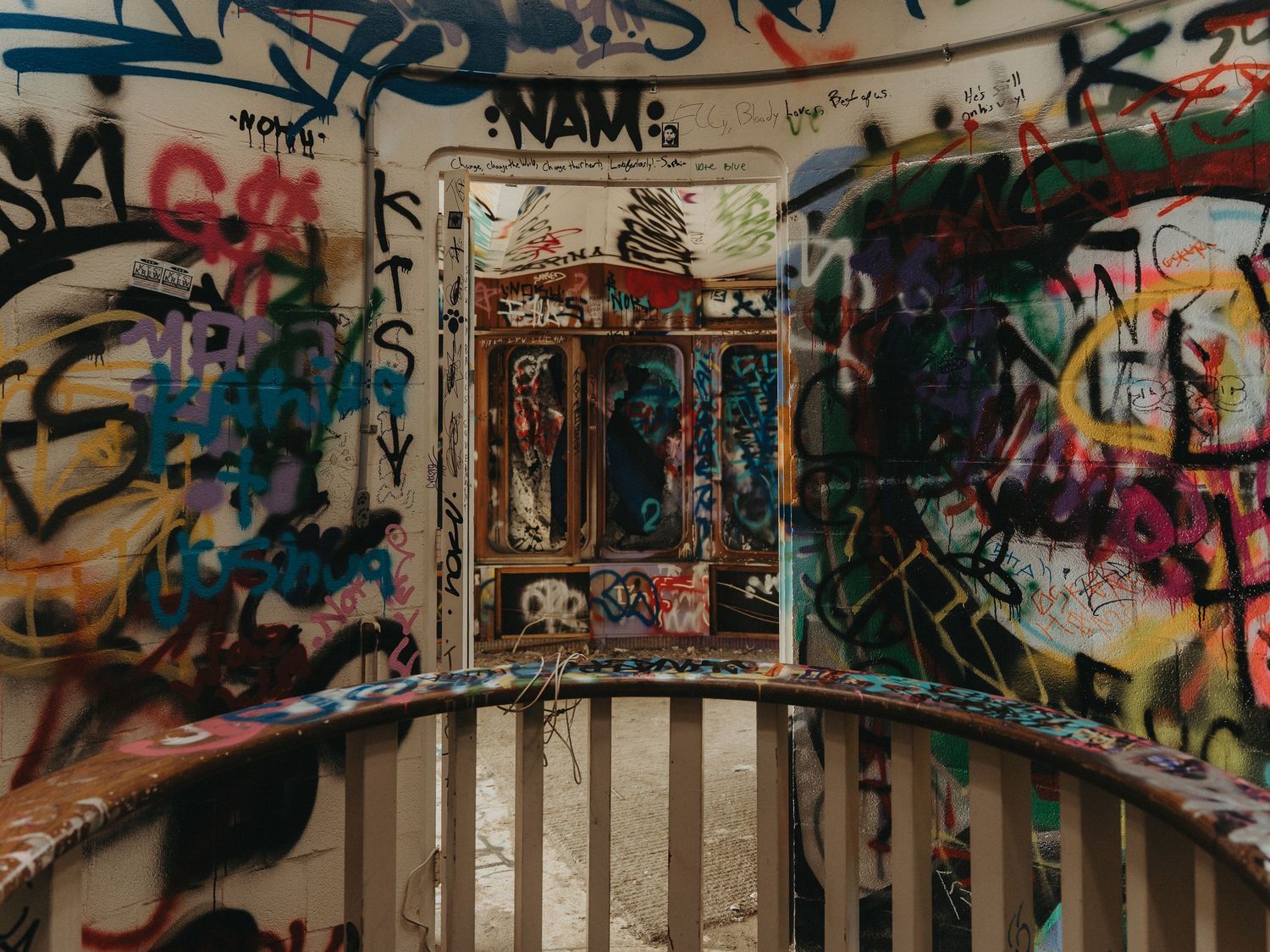 Graffiti-covered wall with an ornate white frame mounted in the center above wooden railing.