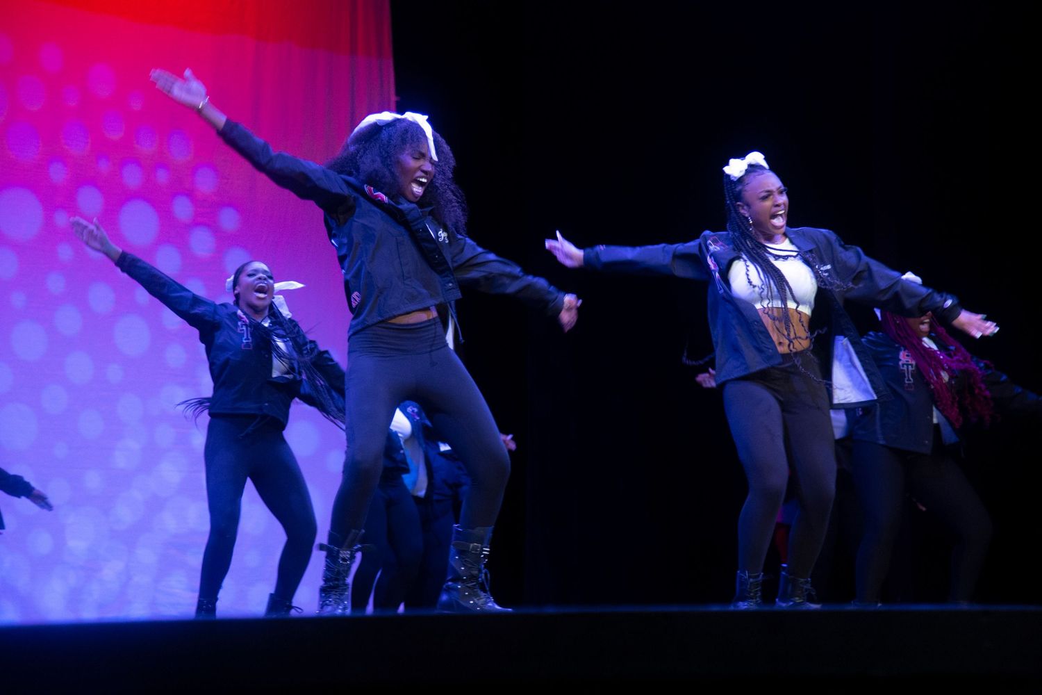 Dance performers on stage with dramatic poses against a purple-lit backdrop.