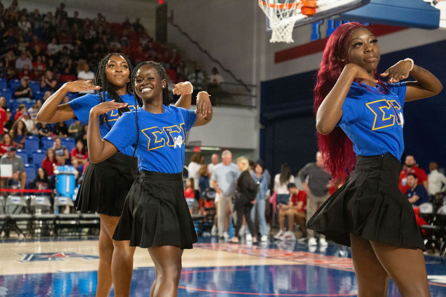 Dance performance team in blue uniforms performing synchronized routine on basketball court.