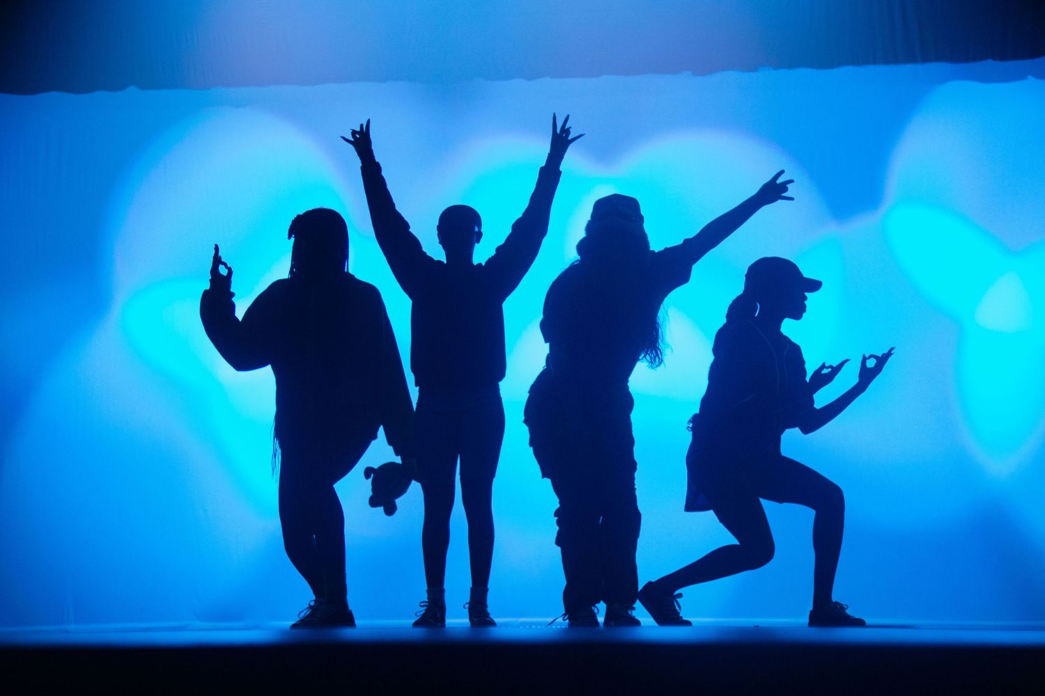 Silhouettes of performers posing against a vibrant blue backdrop during a show.