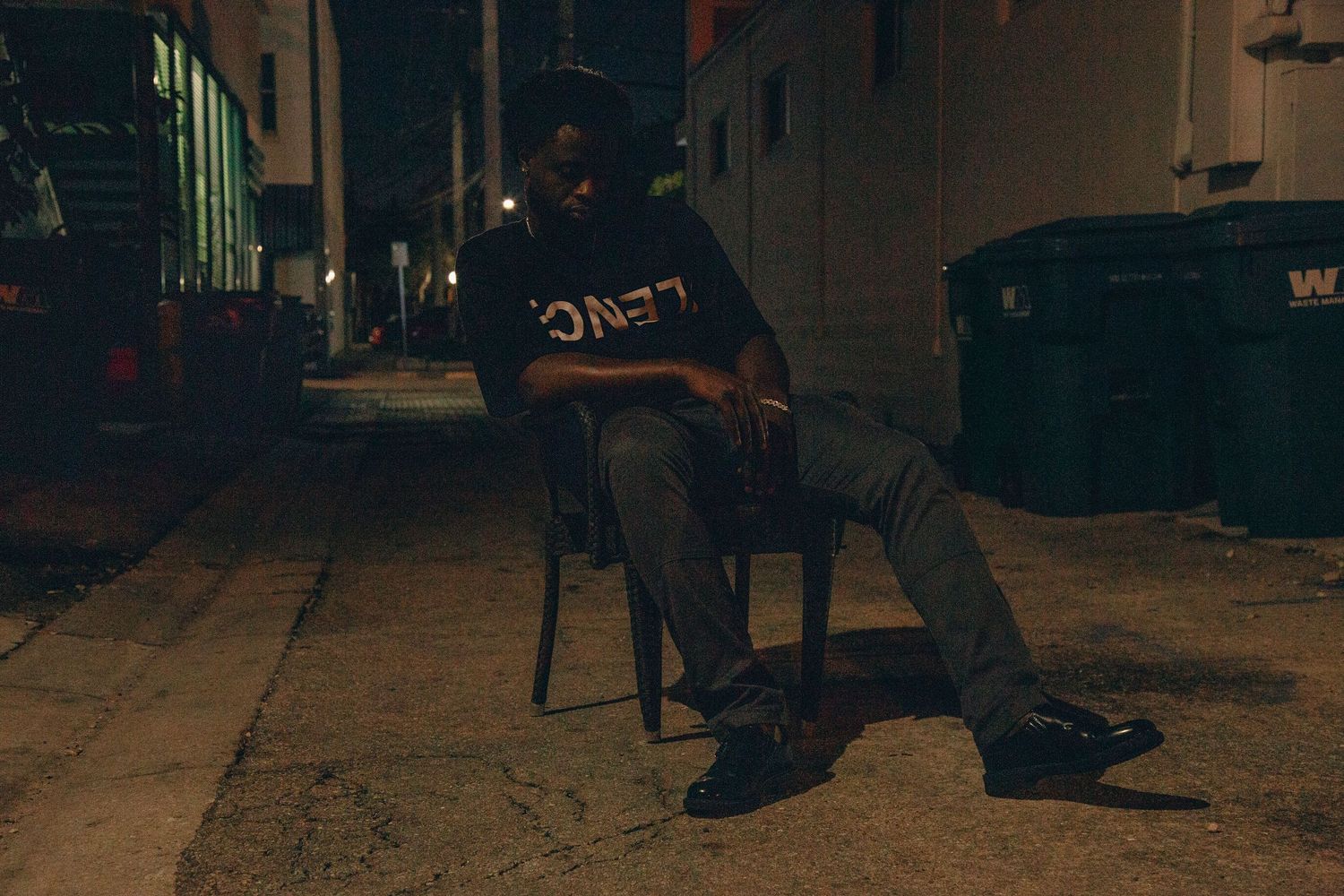 Person in black shirt sitting on chair in dark alley.