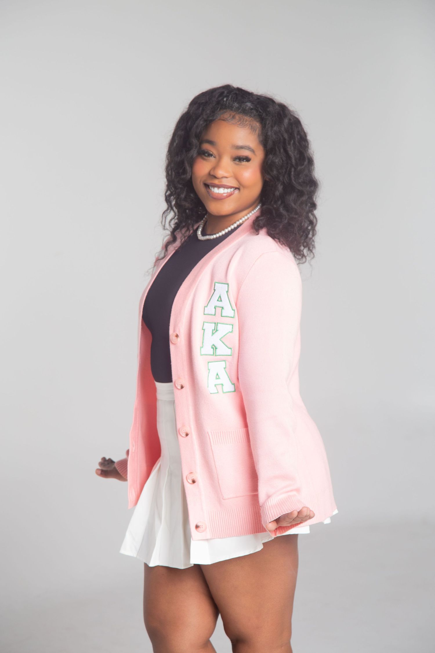 Person in pink sorority cardigan and white skirt poses against white background.