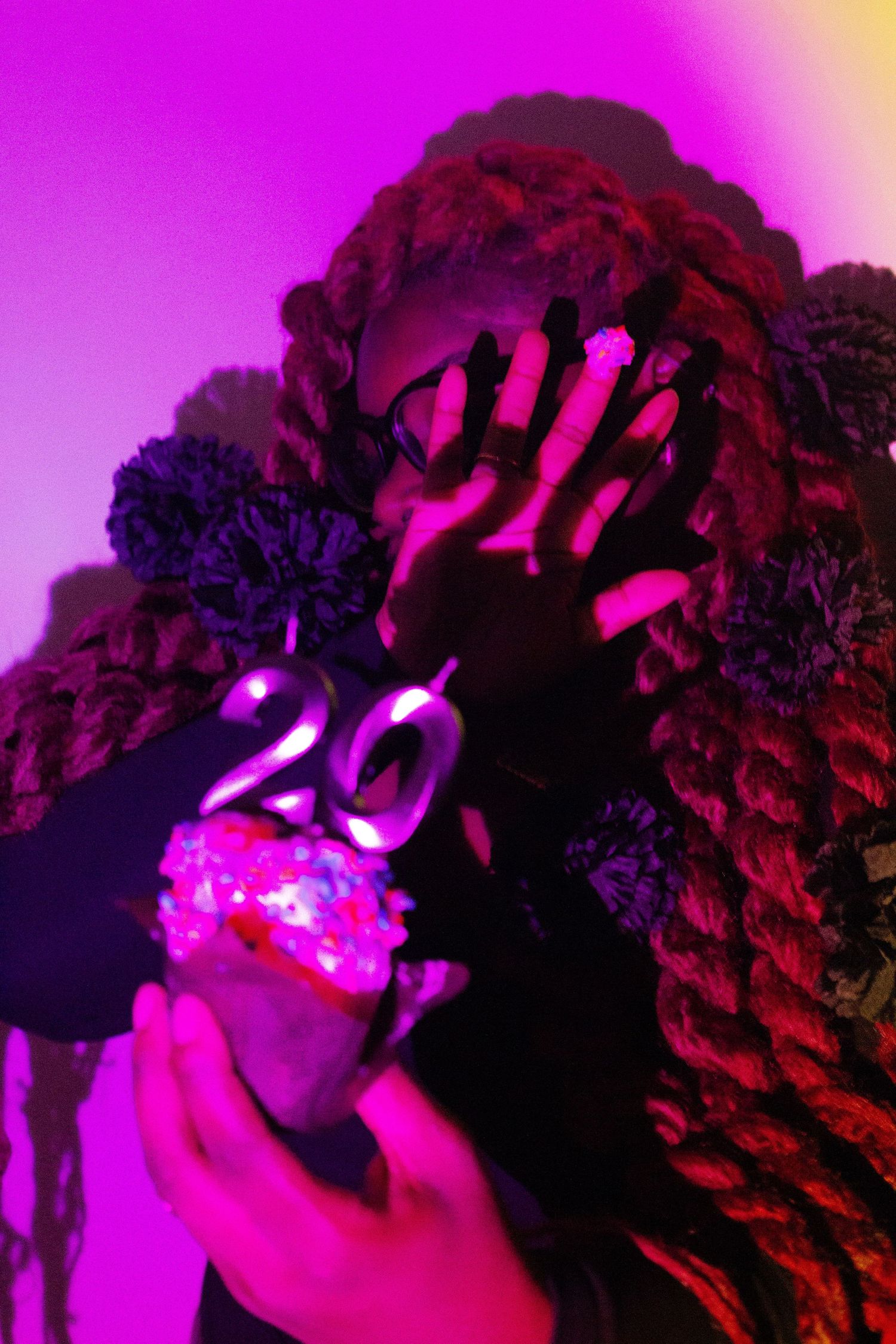 Hand holding illuminated number 20 against purple and pink backdrop.
