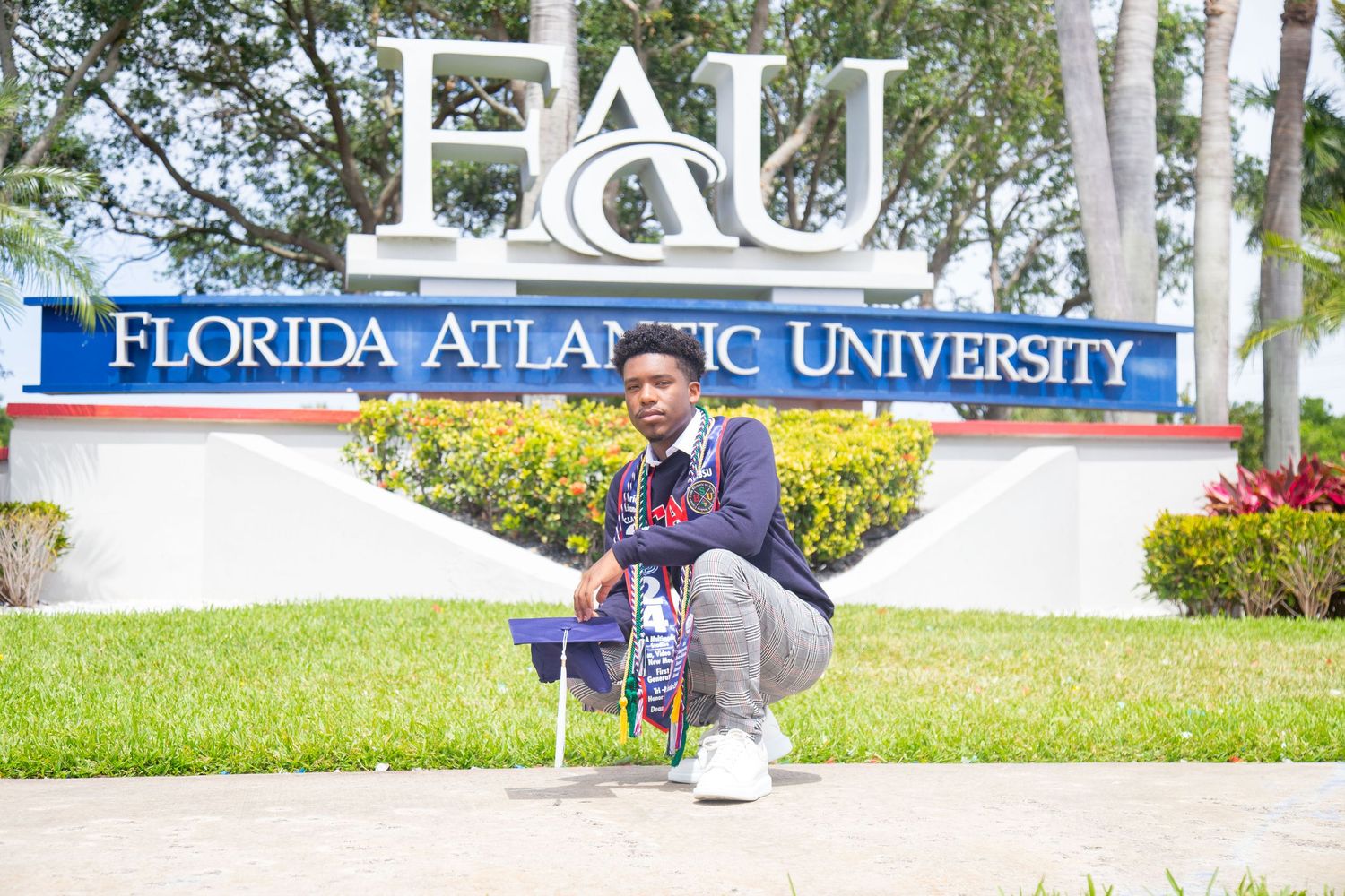 Graduate poses in front of Florida Atlantic University entrance sign wearing graduation regalia.