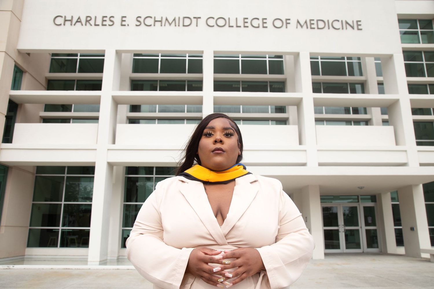 Professional portrait of graduate in white coat outside Charles E. Schmidt College of Medicine building.