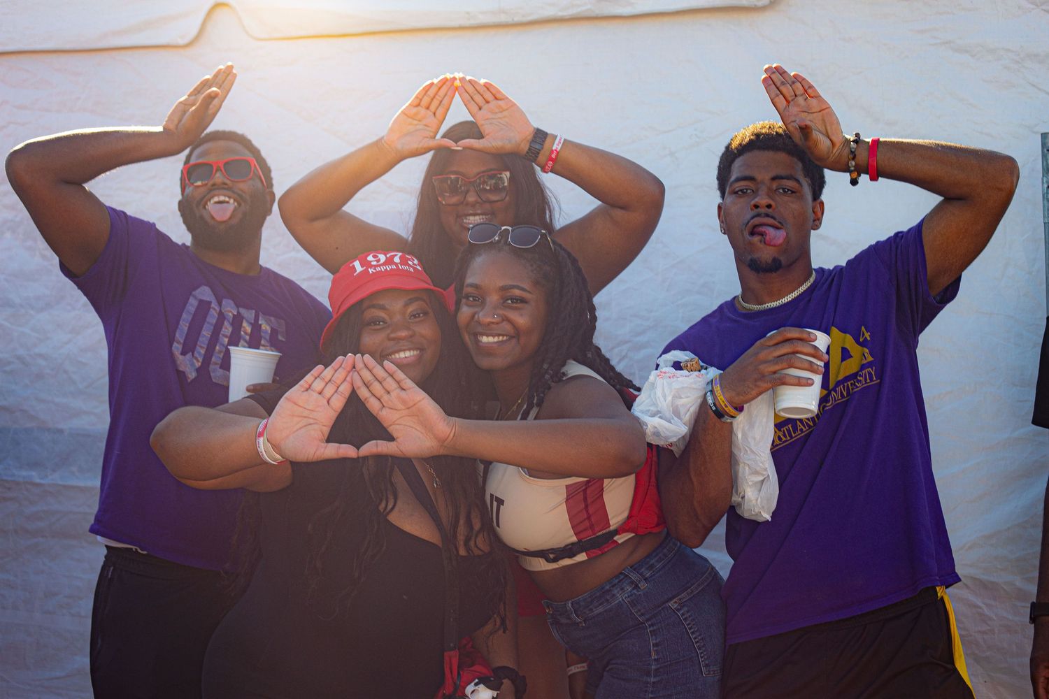 Group of people celebrating with raised arms against a white wall background.
