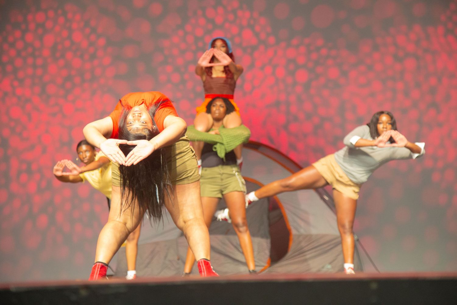 Dancers performing a dynamic dance routine on stage with a red spotlit background.