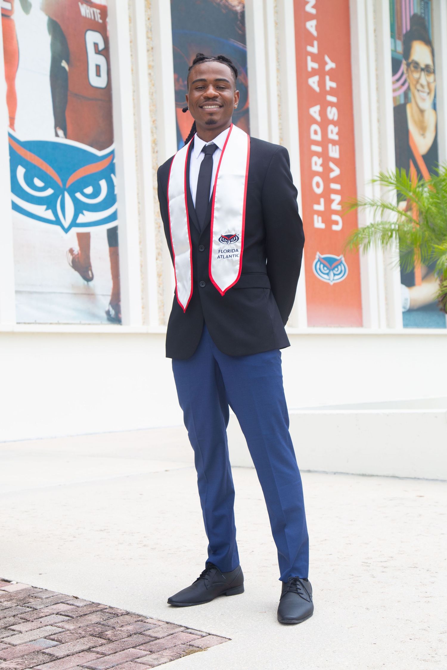 Graduate in formal attire poses in front of university wall with owl logo.