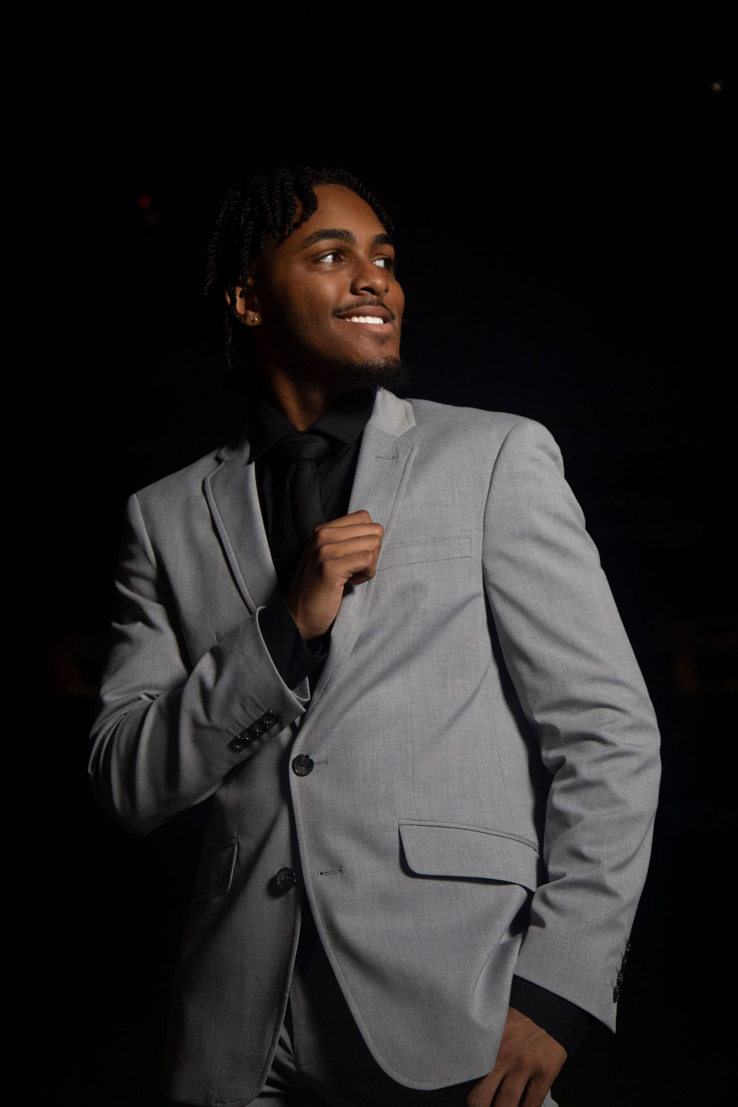A person wearing a light gray blazer poses against a dark background in a series of artistic portrait shots.