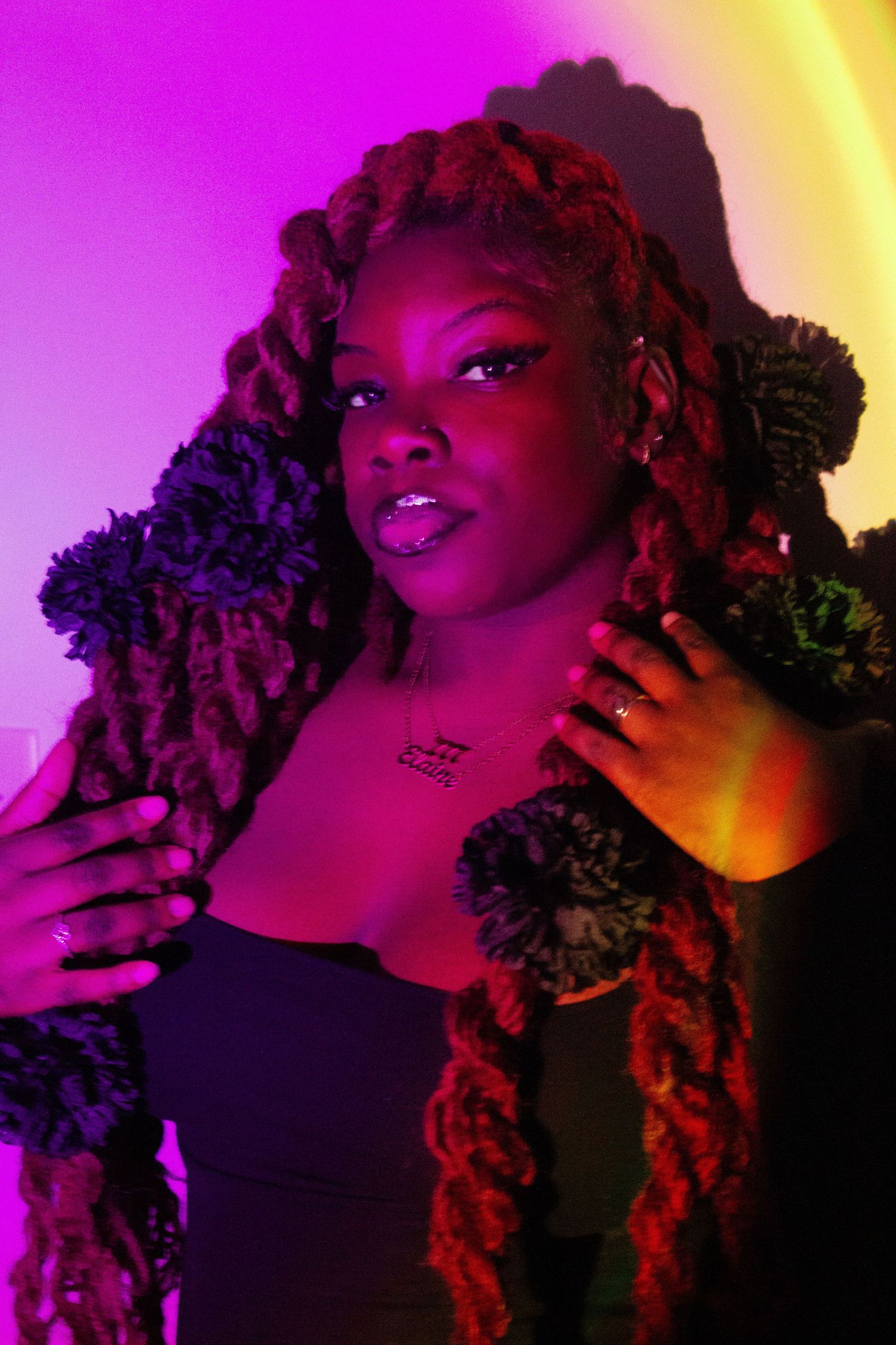 Artistic portrait with vibrant pink and purple lighting highlighting long braided hairstyle.
