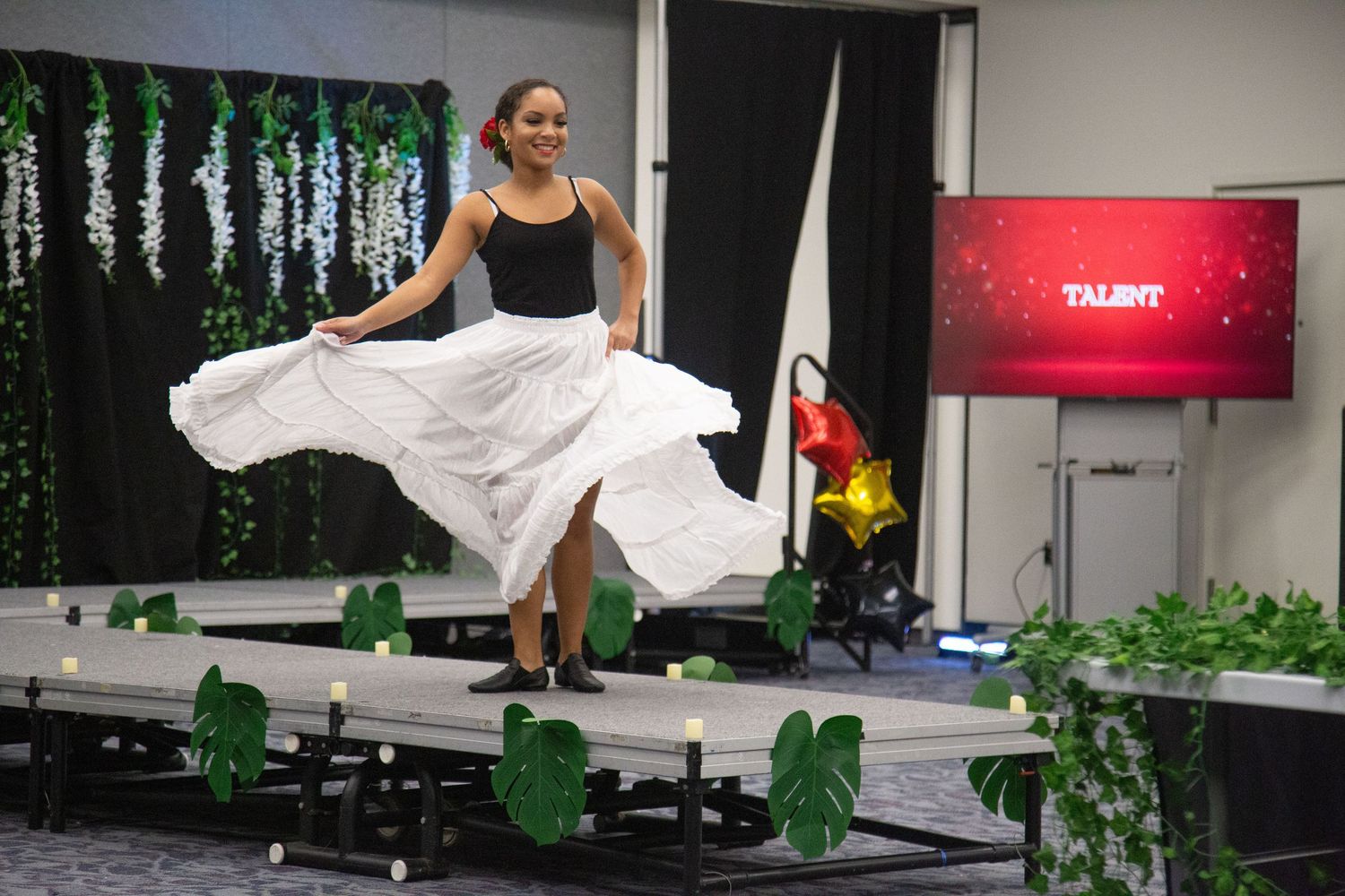 Dancer in black top and flowing white skirt performing on decorated stage.