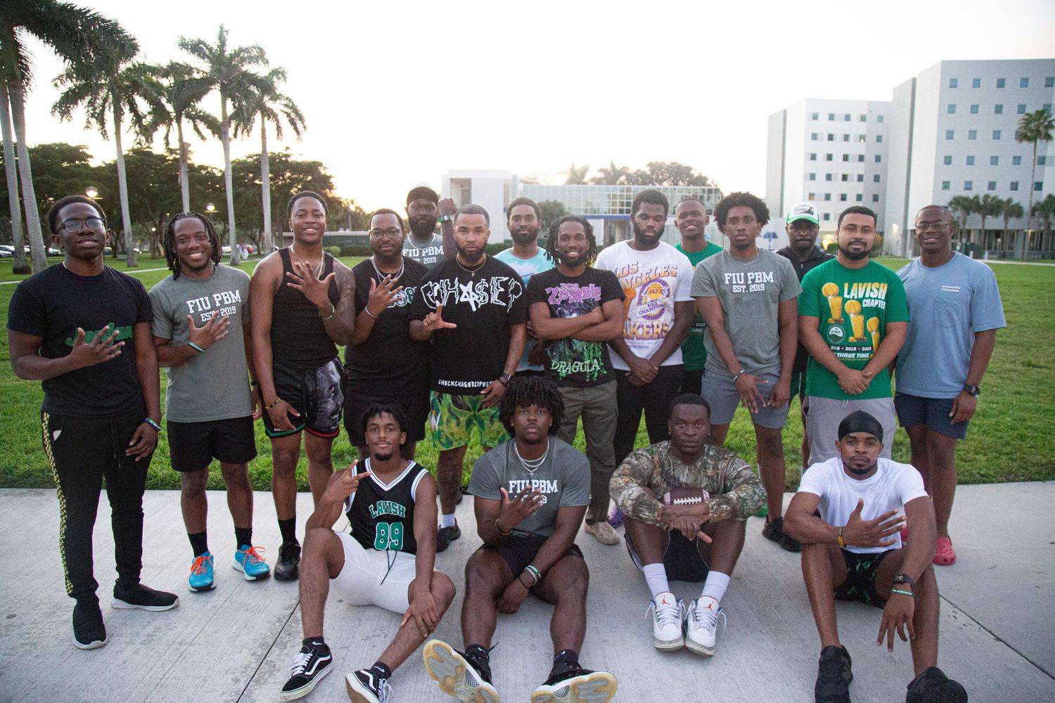 Group photo of students gathered outdoors on campus with palm trees in background.