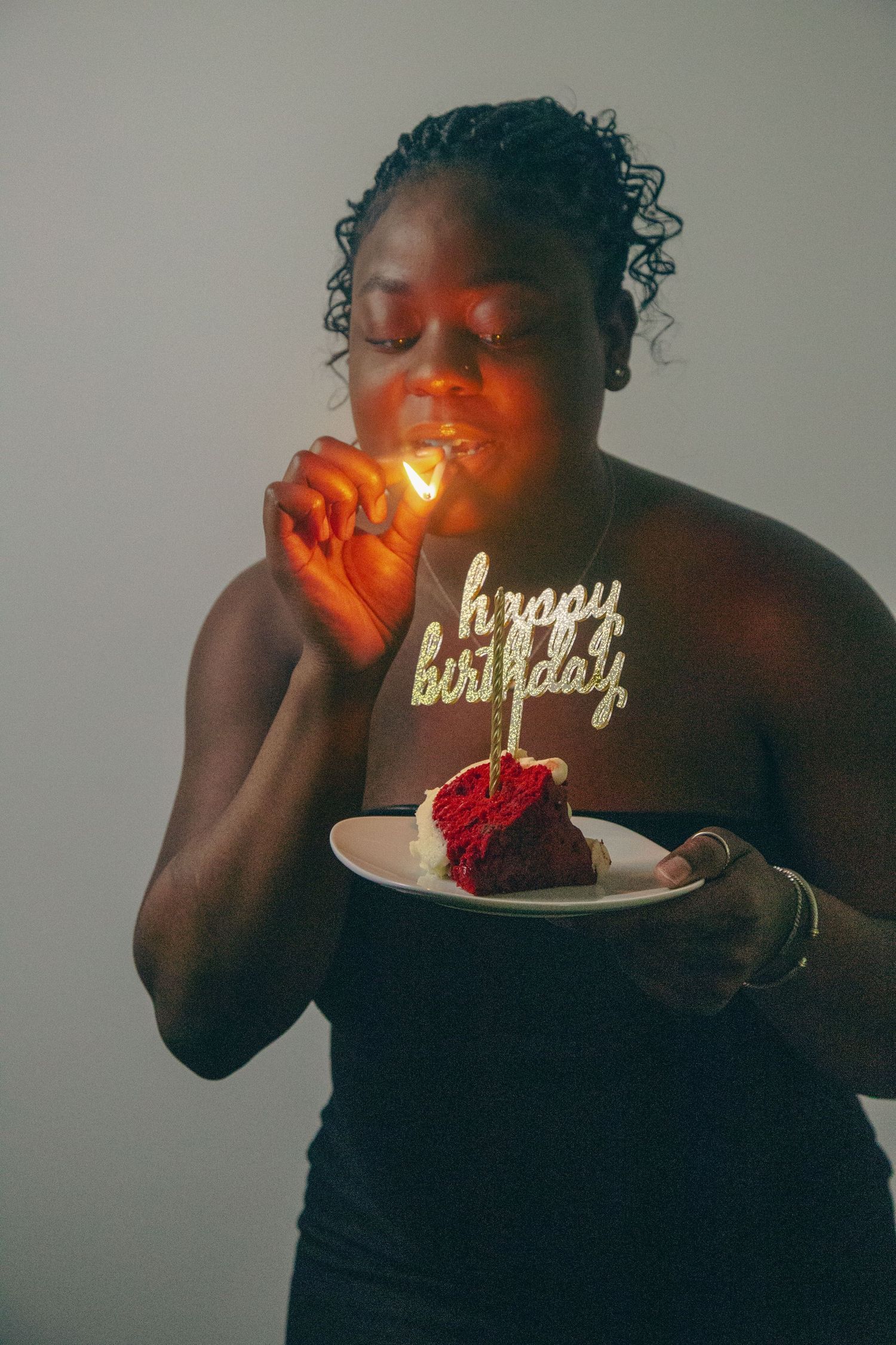 Person in black dress lighting birthday candle on red cake slice.