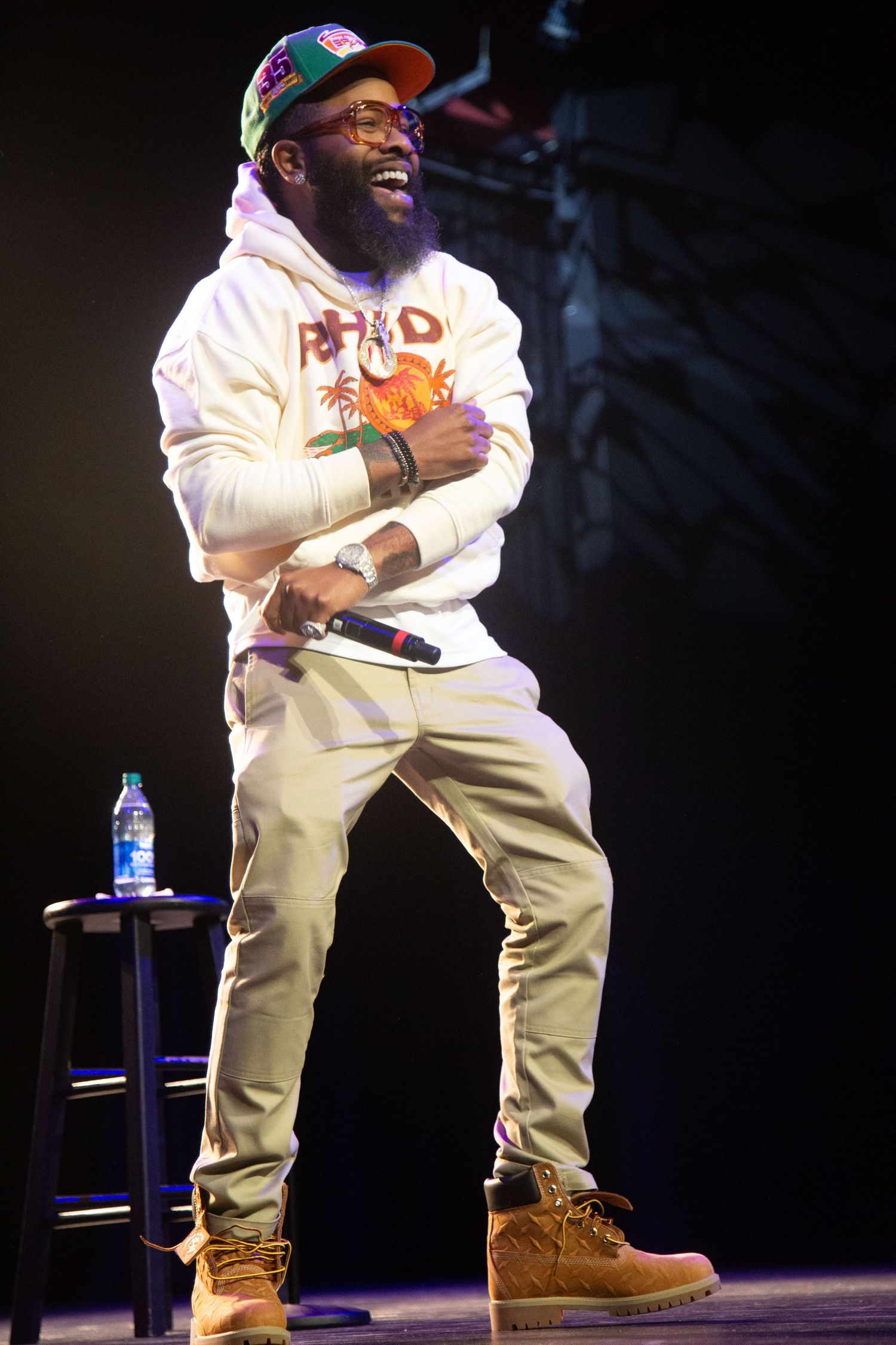 Performer in a white outfit and brown boots entertains an audience on stage during a live show.