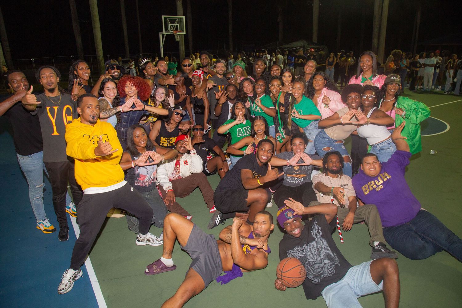 Large group poses together on outdoor basketball court during nighttime community gathering or event.