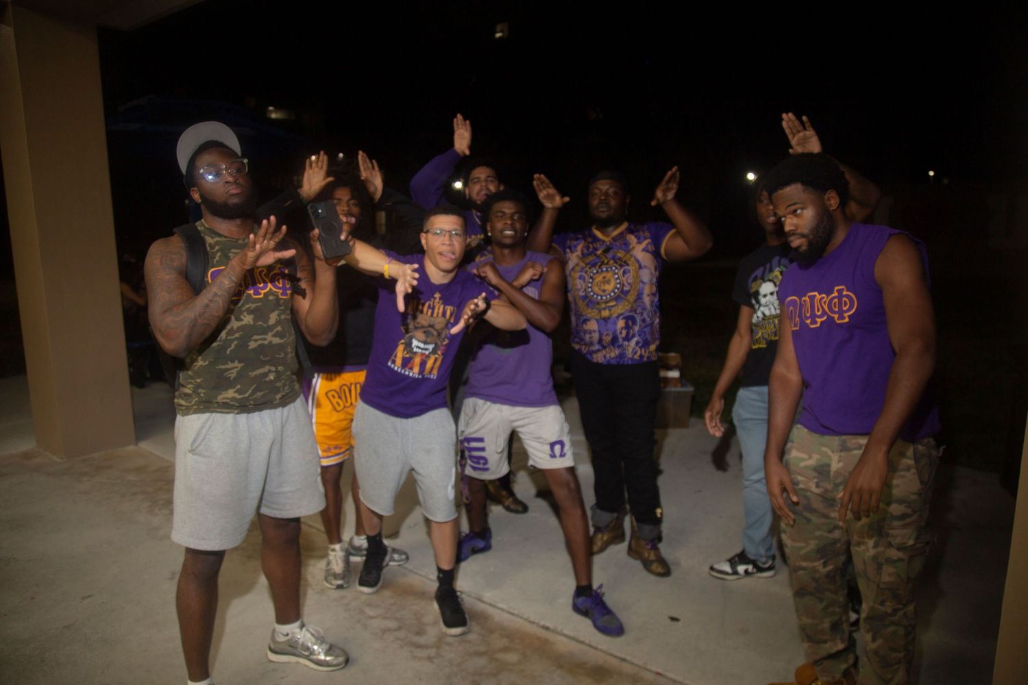 A group of people dancing and celebrating outdoors at night wearing purple and white clothing.