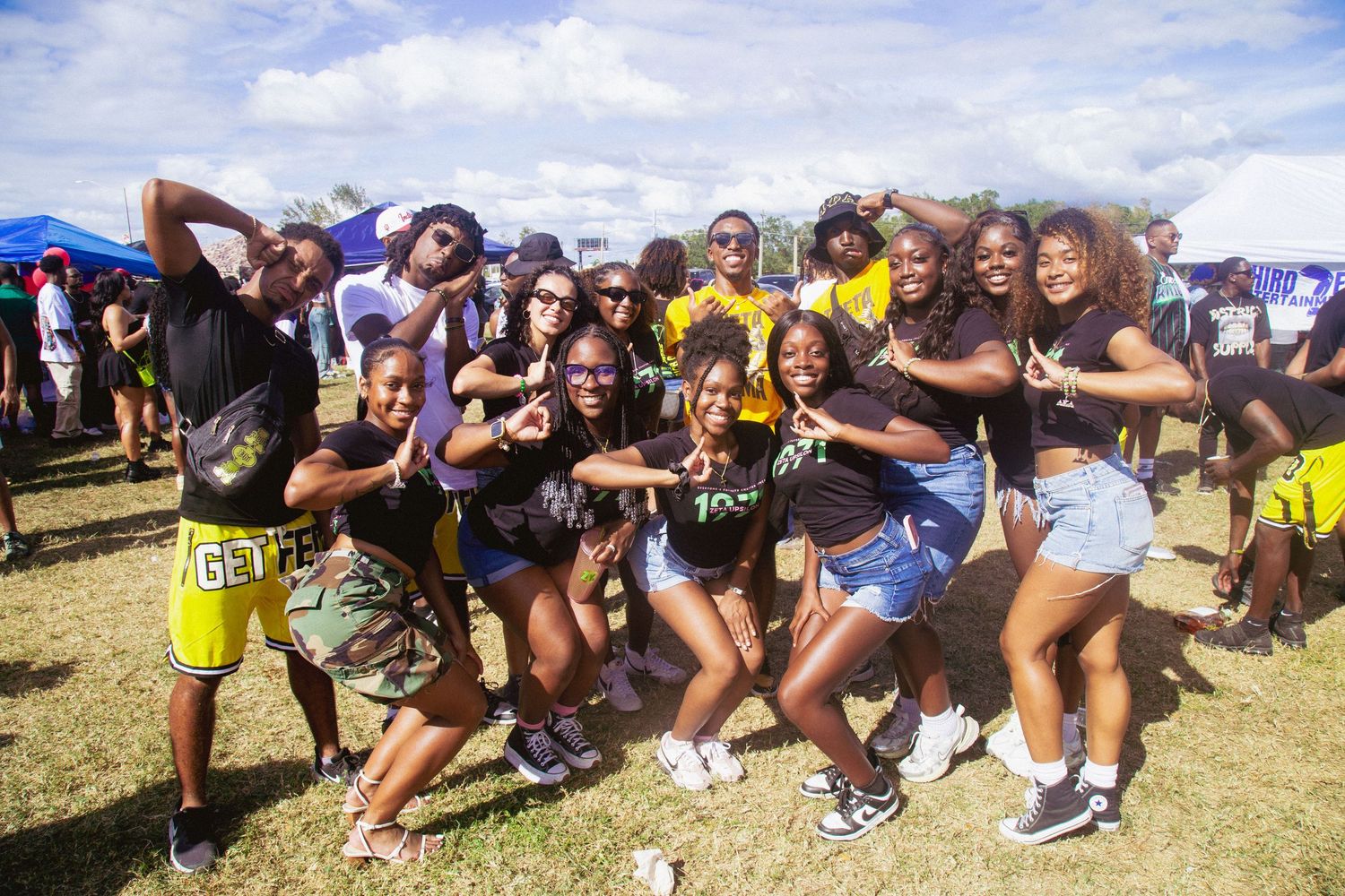 A group poses for a photo wearing various black and gold and black, green and pink outfits.