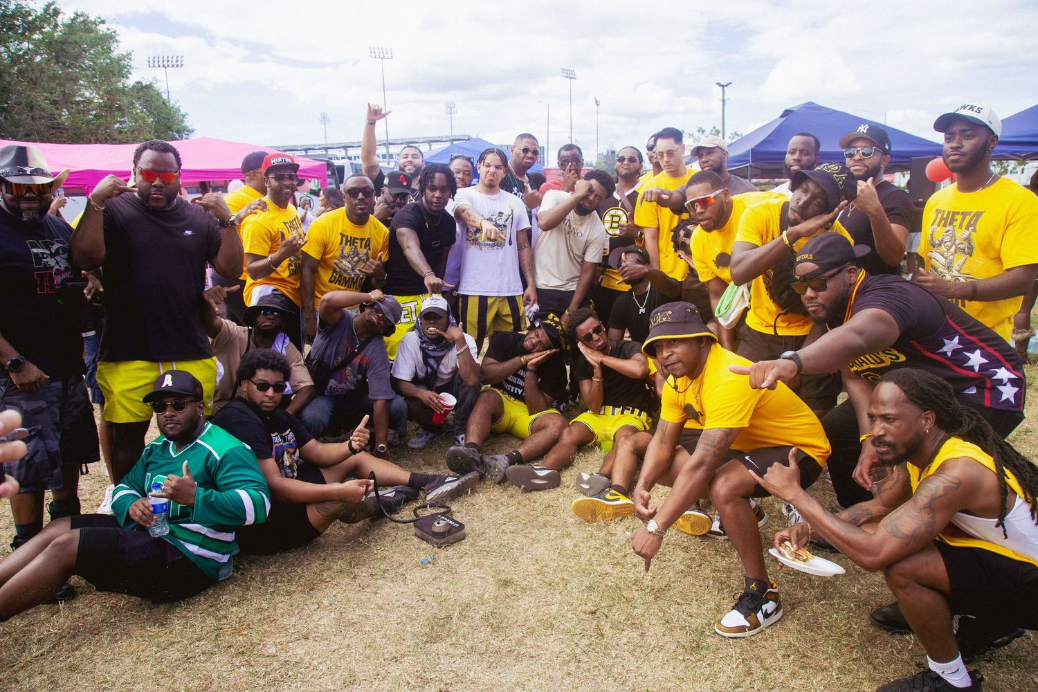 Large outdoor group gathering with people in yellow and dark clothing sitting on grass.