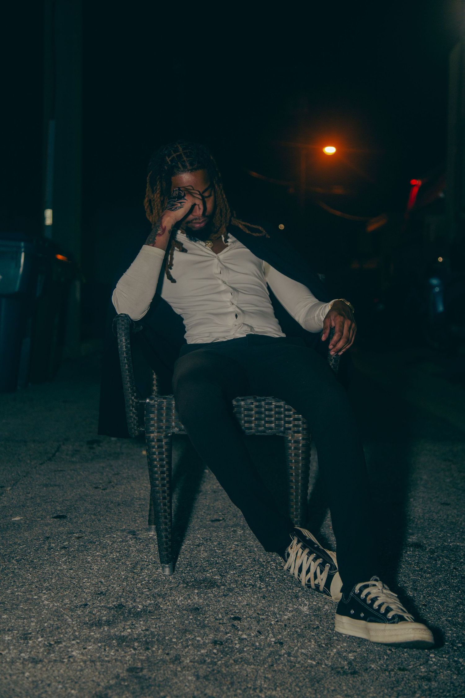 Figure seated in dark chair at night wearing white button-up shirt and black pants.
