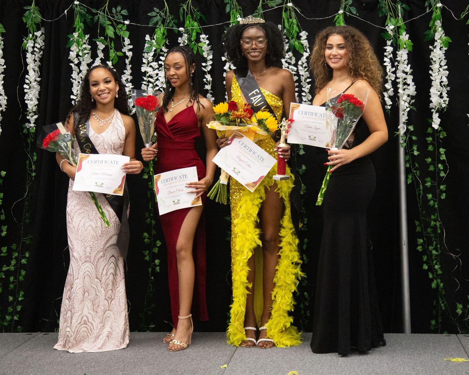 Formal group photo with people wearing elegant dresses against a backdrop with hanging greenery.