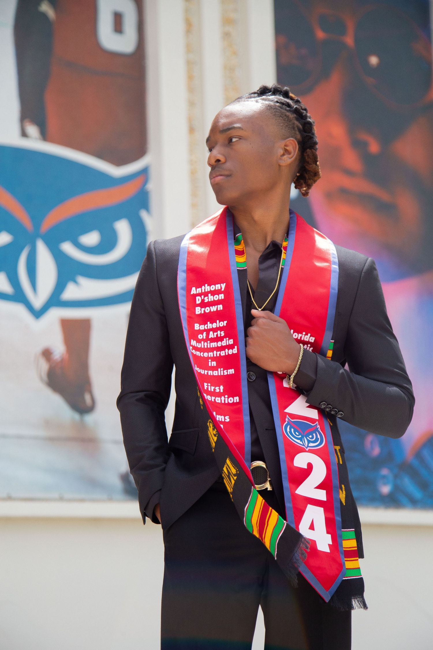 Graduate wearing graduation stole with academic honors stands before university wall with owl design.