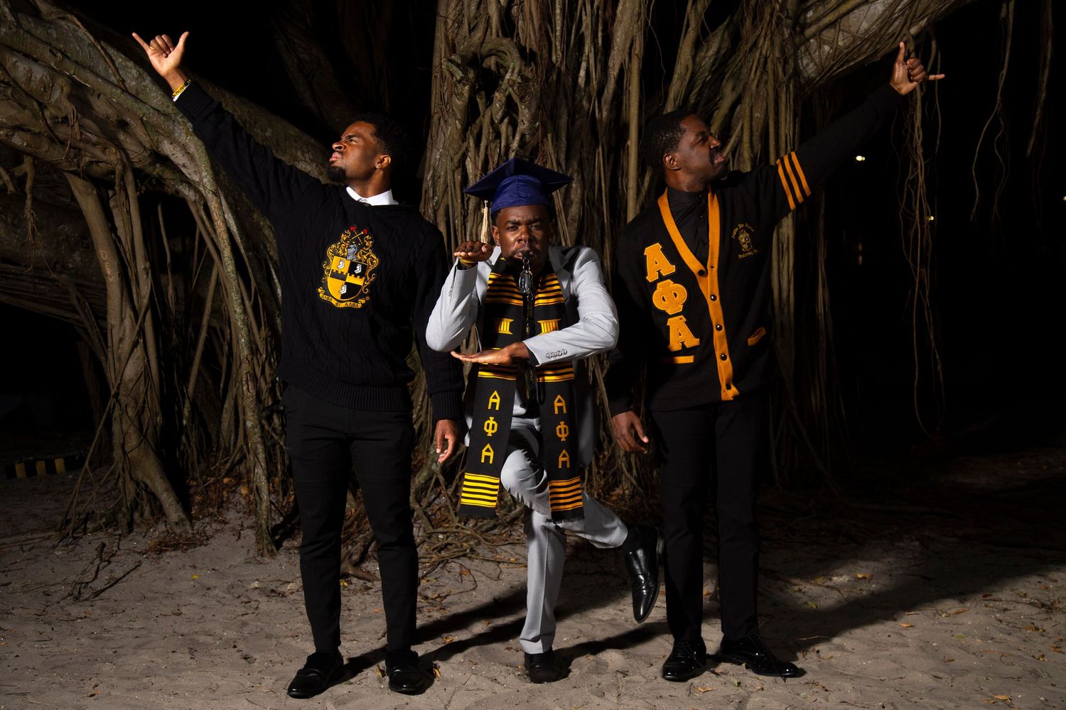 Nighttime graduation photos among banyan trees with graduates wearing academic regalia.