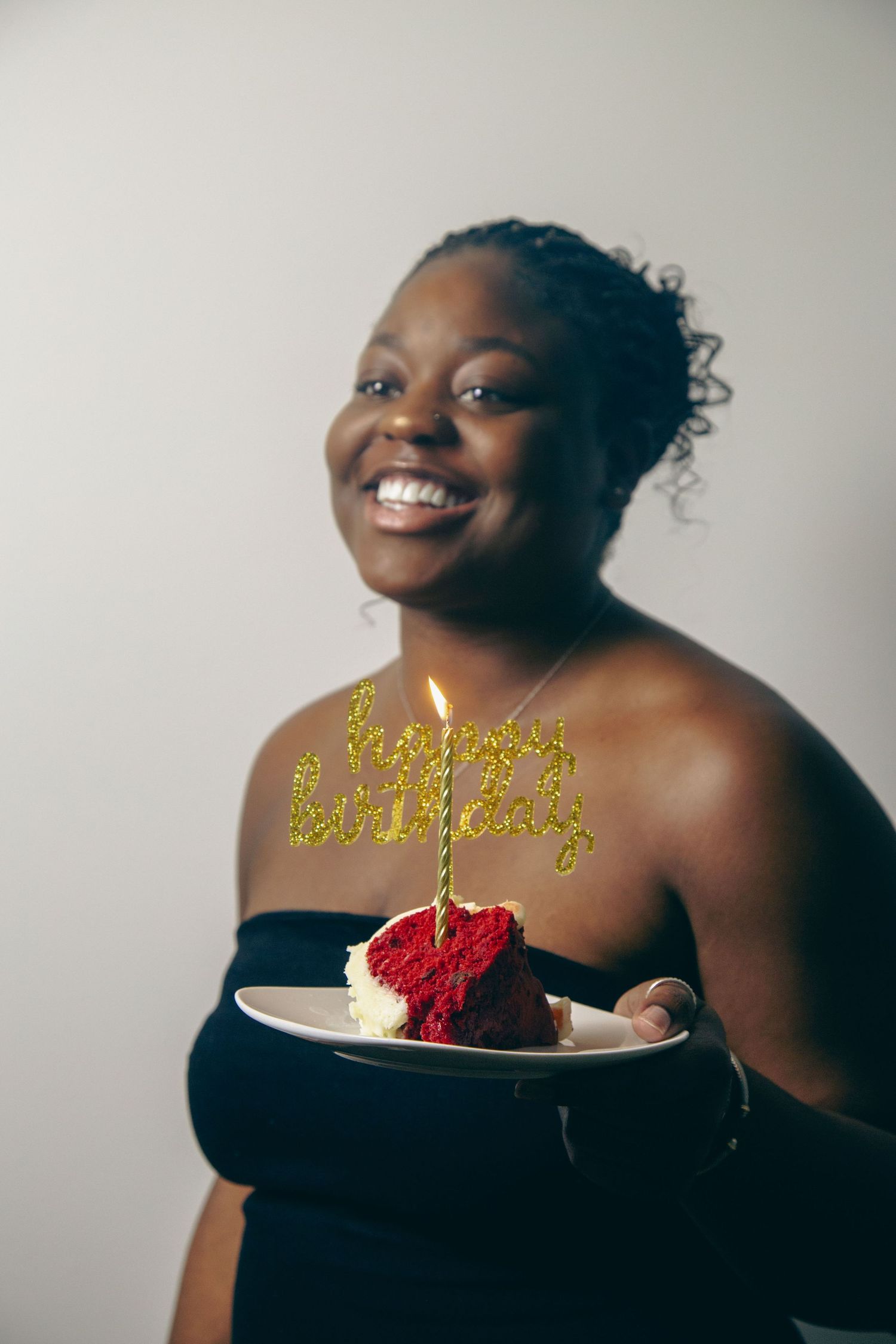 Person in black dress smiling with birthday cake and glowing golden text.