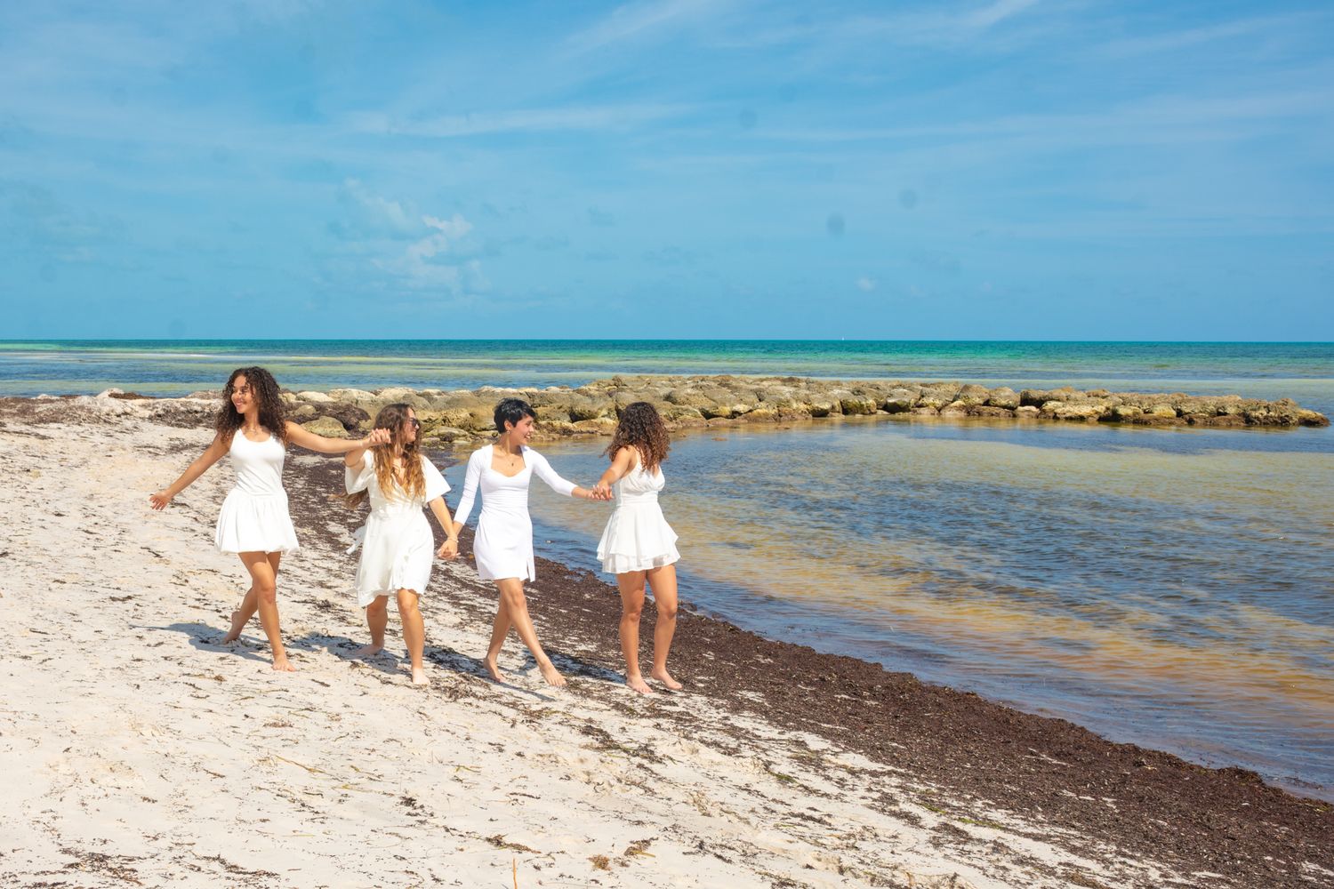 Group walking together along tropical beach shoreline wearing coordinated white outfits.