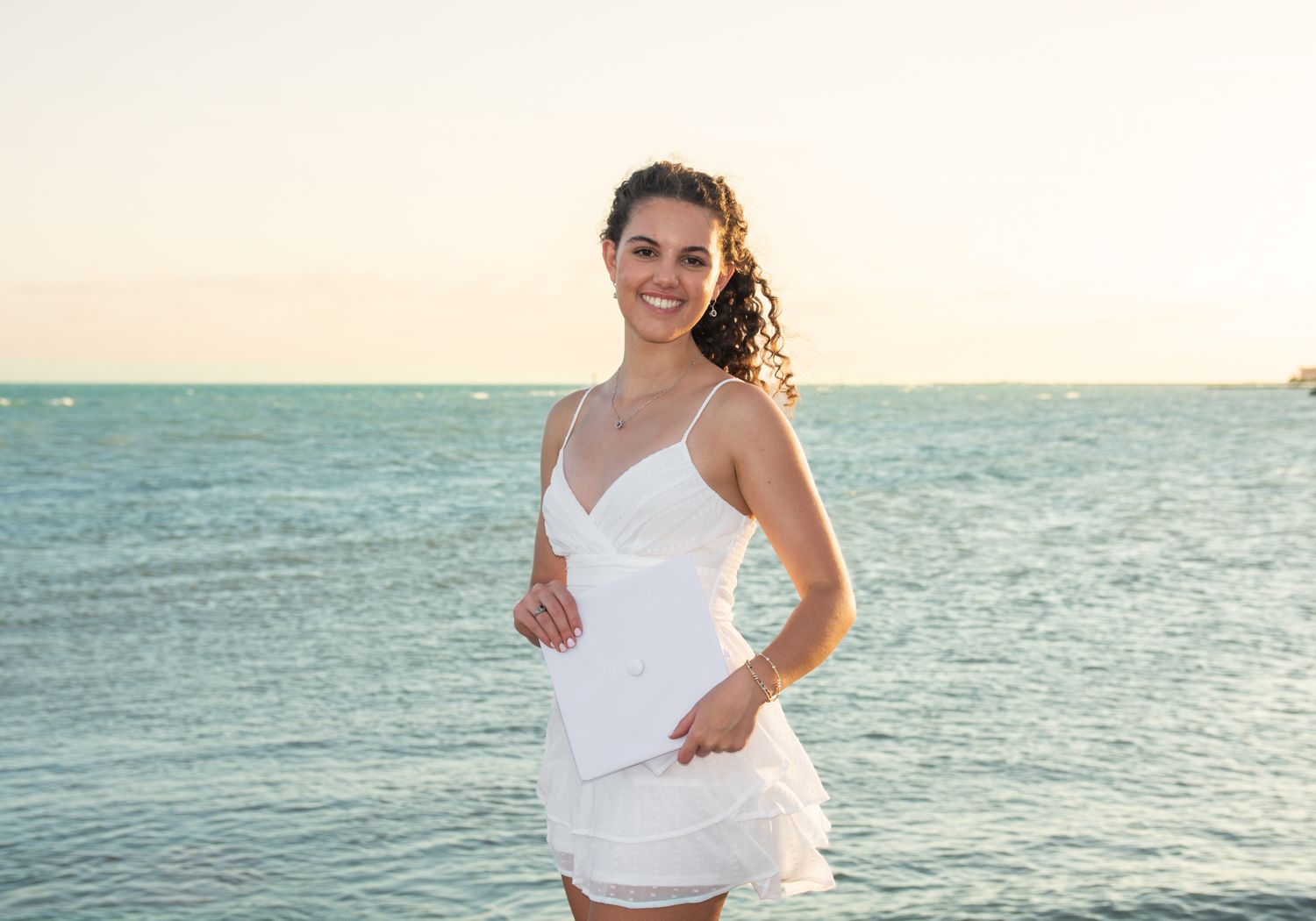 Beachside portrait in white dress with ocean waves and sunset in background.