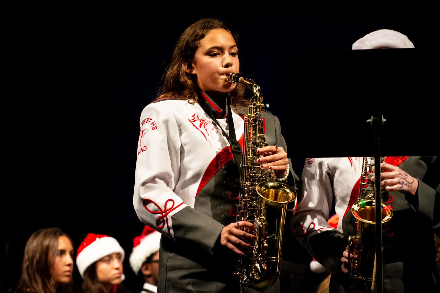 Saxophonist performs in holiday concert setting with other musicians in background.